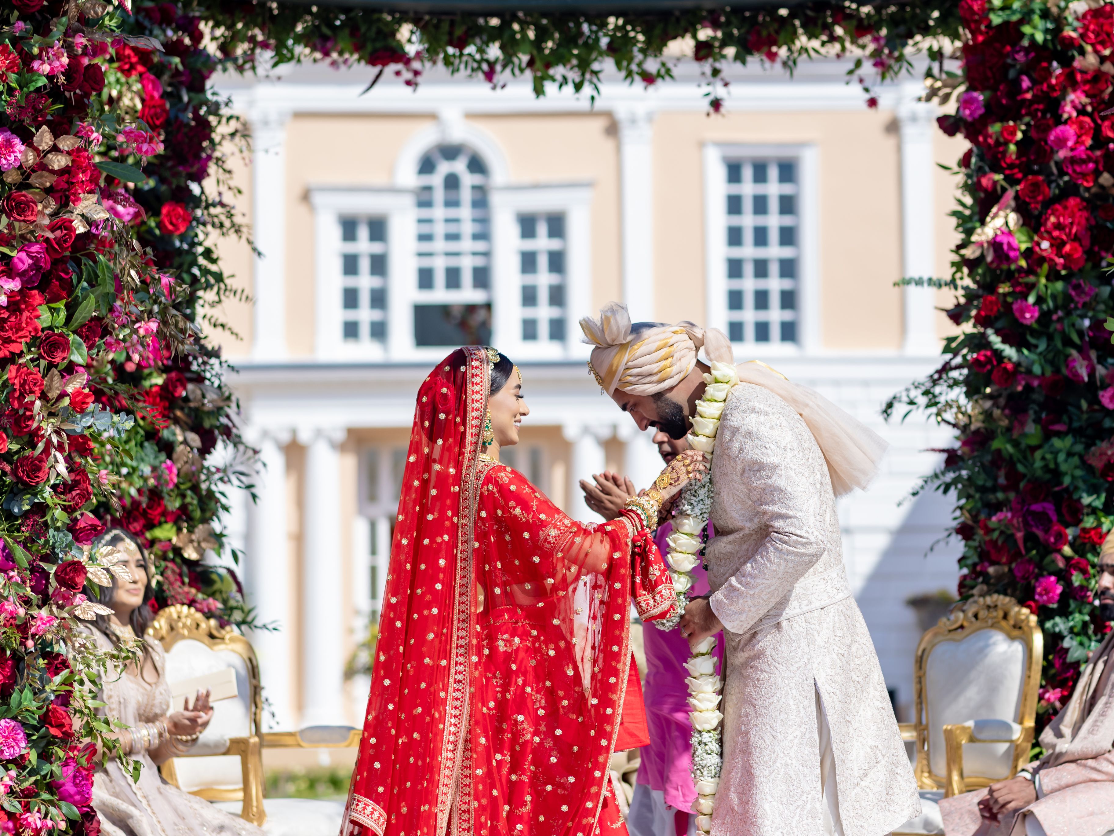 Indian wedding ceremony outdoors under floral arch with bride and groom exchanging garlands