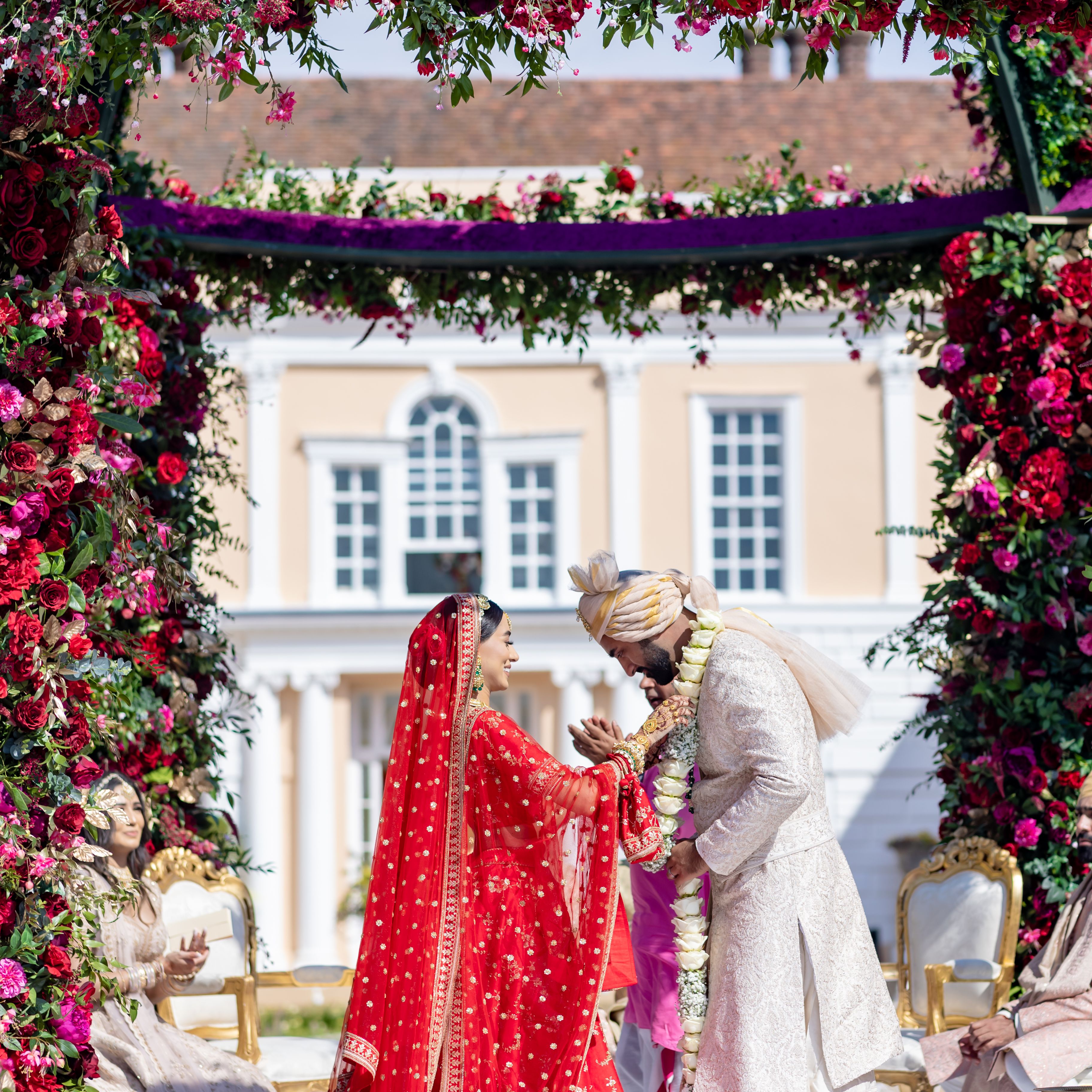 Indian wedding ceremony outdoors under floral arch with bride and groom exchanging garlands