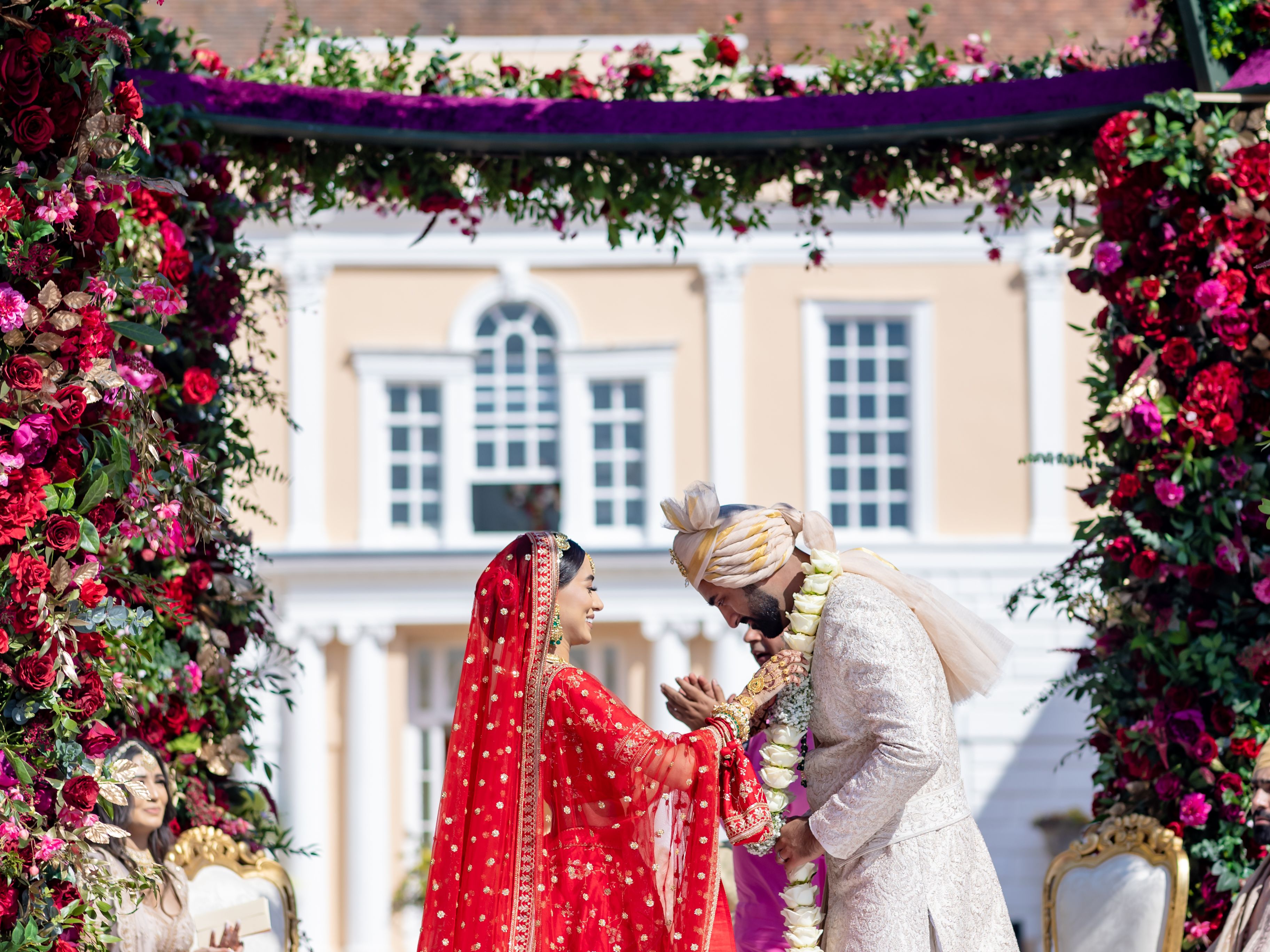 Indian wedding ceremony outdoors under floral arch with bride and groom exchanging garlands