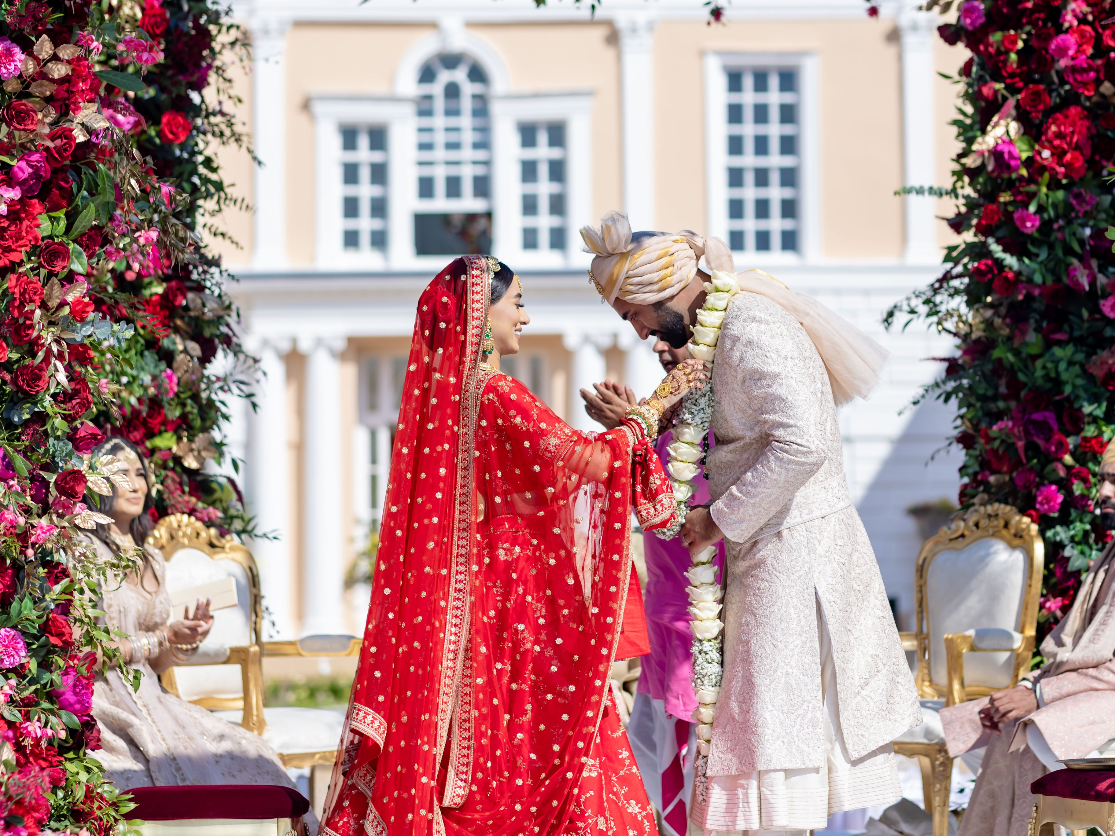 Indian wedding ceremony outdoors under floral arch with bride and groom exchanging garlands