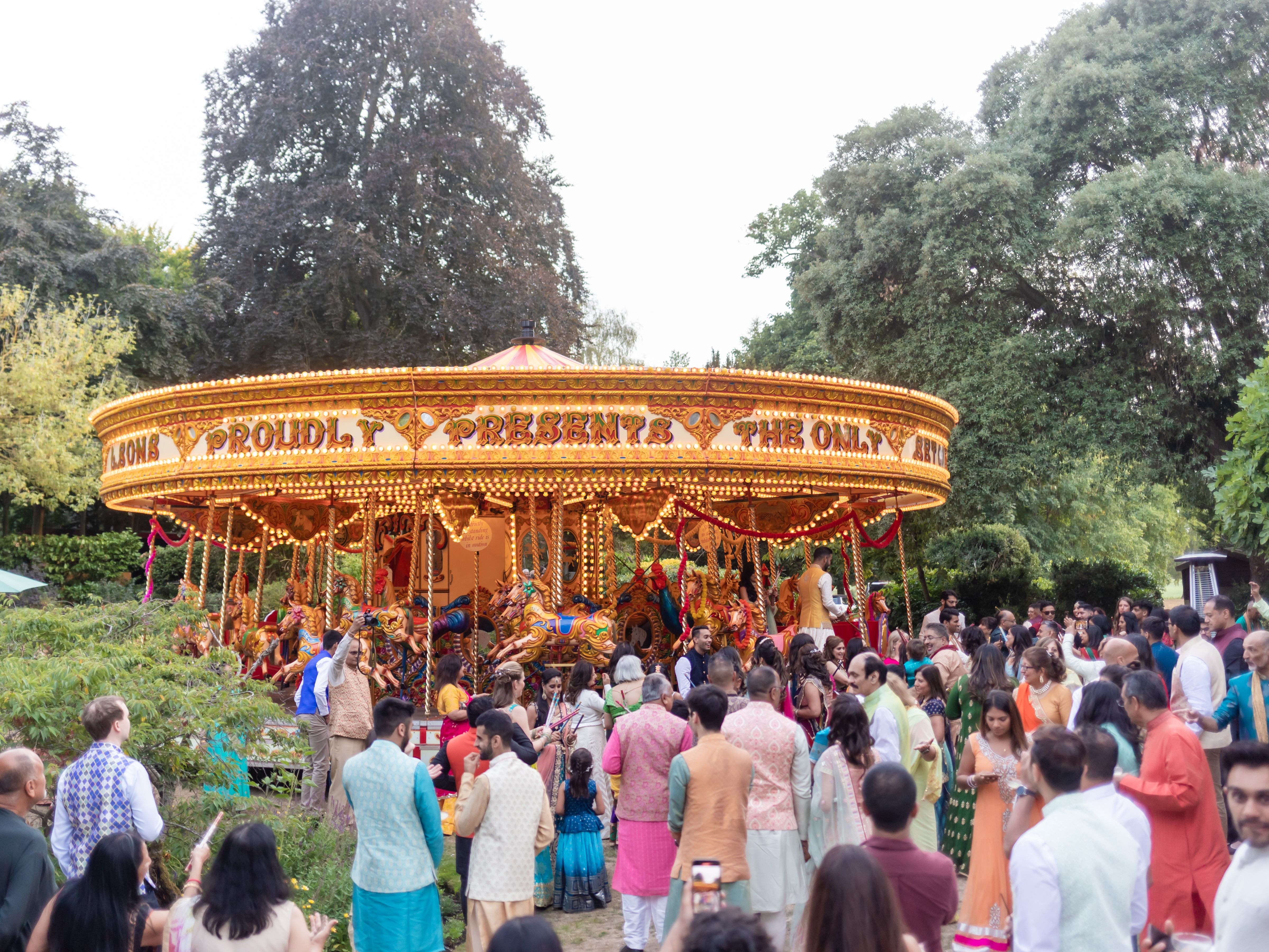 A vibrant crowd gathers around an illuminated vintage carousel at an outdoor event.