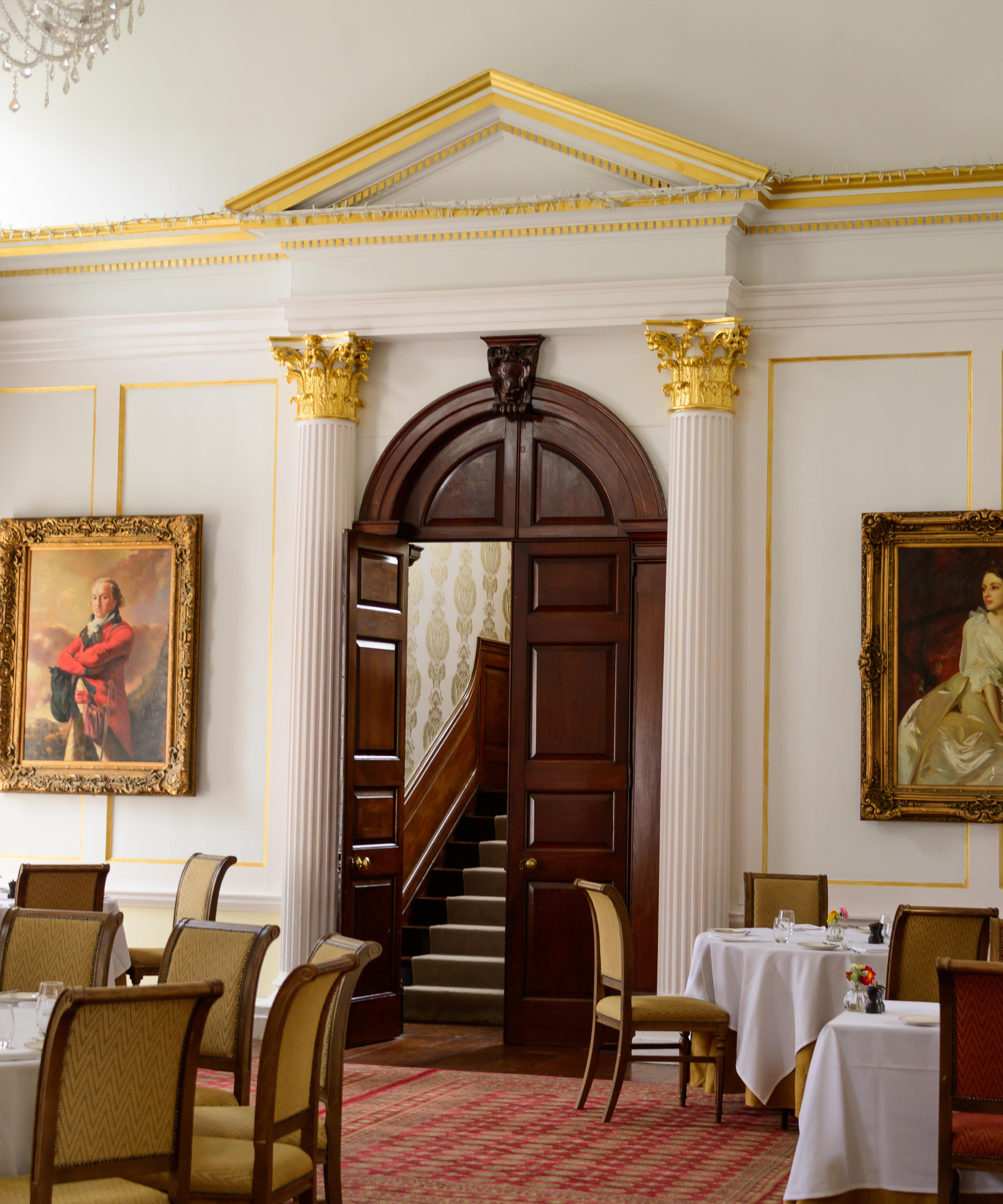 Elegant dining room with classic decor, large portraits, and wooden door leading to a staircase