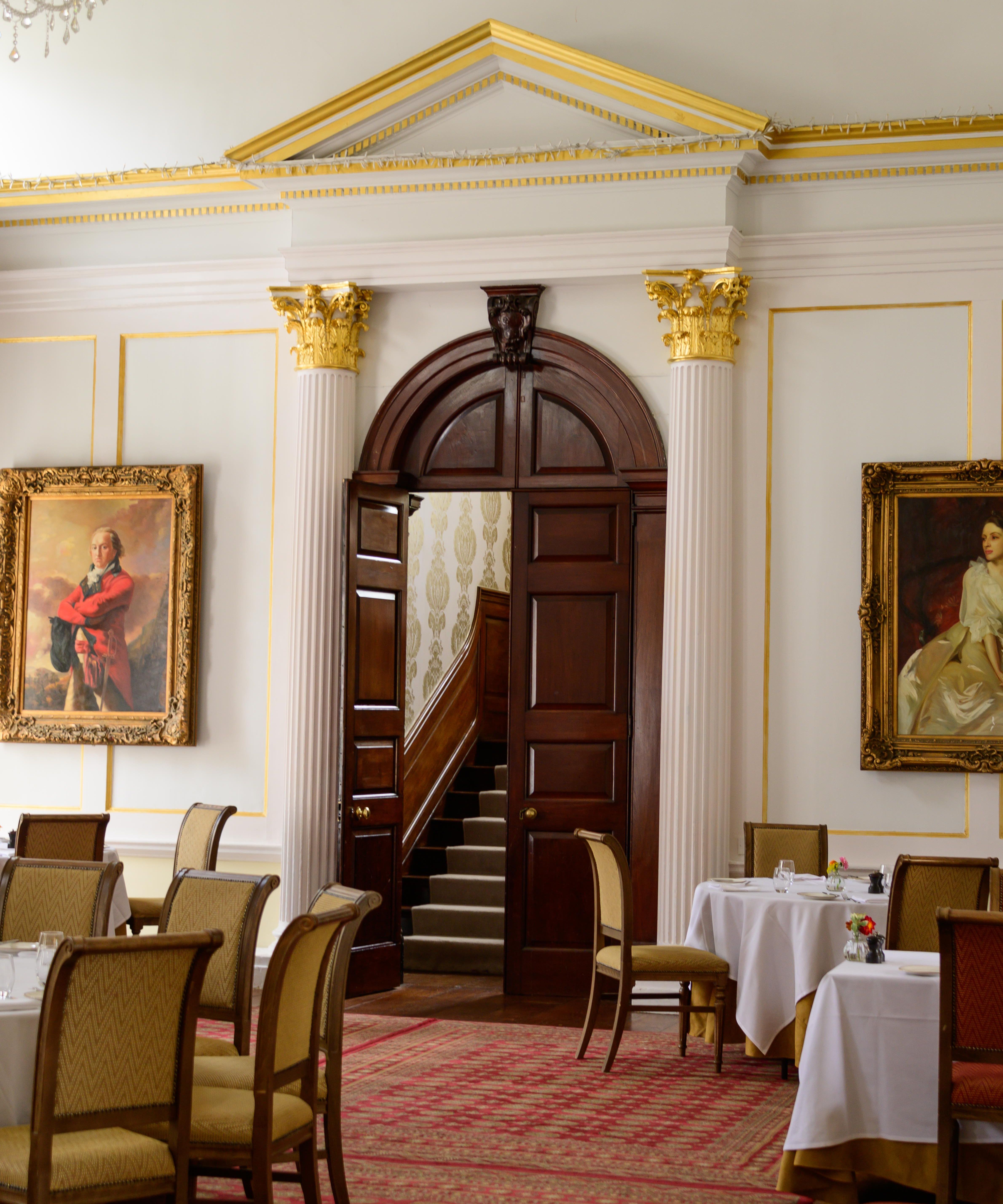 Elegant dining room with classic decor, large portraits, and wooden door leading to a staircase