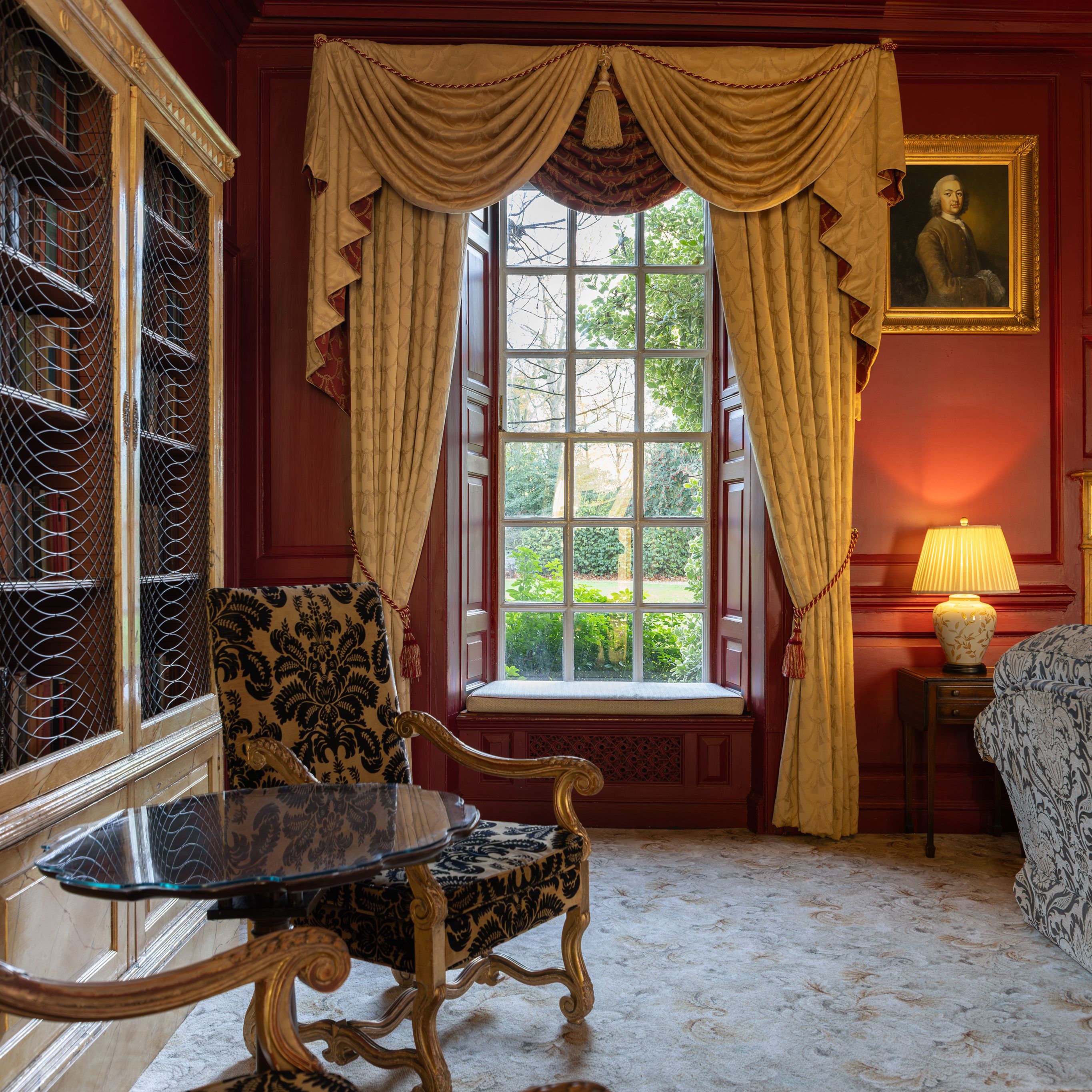 Elegant traditional living room with ornate furniture, large window, red walls, and classic decor.