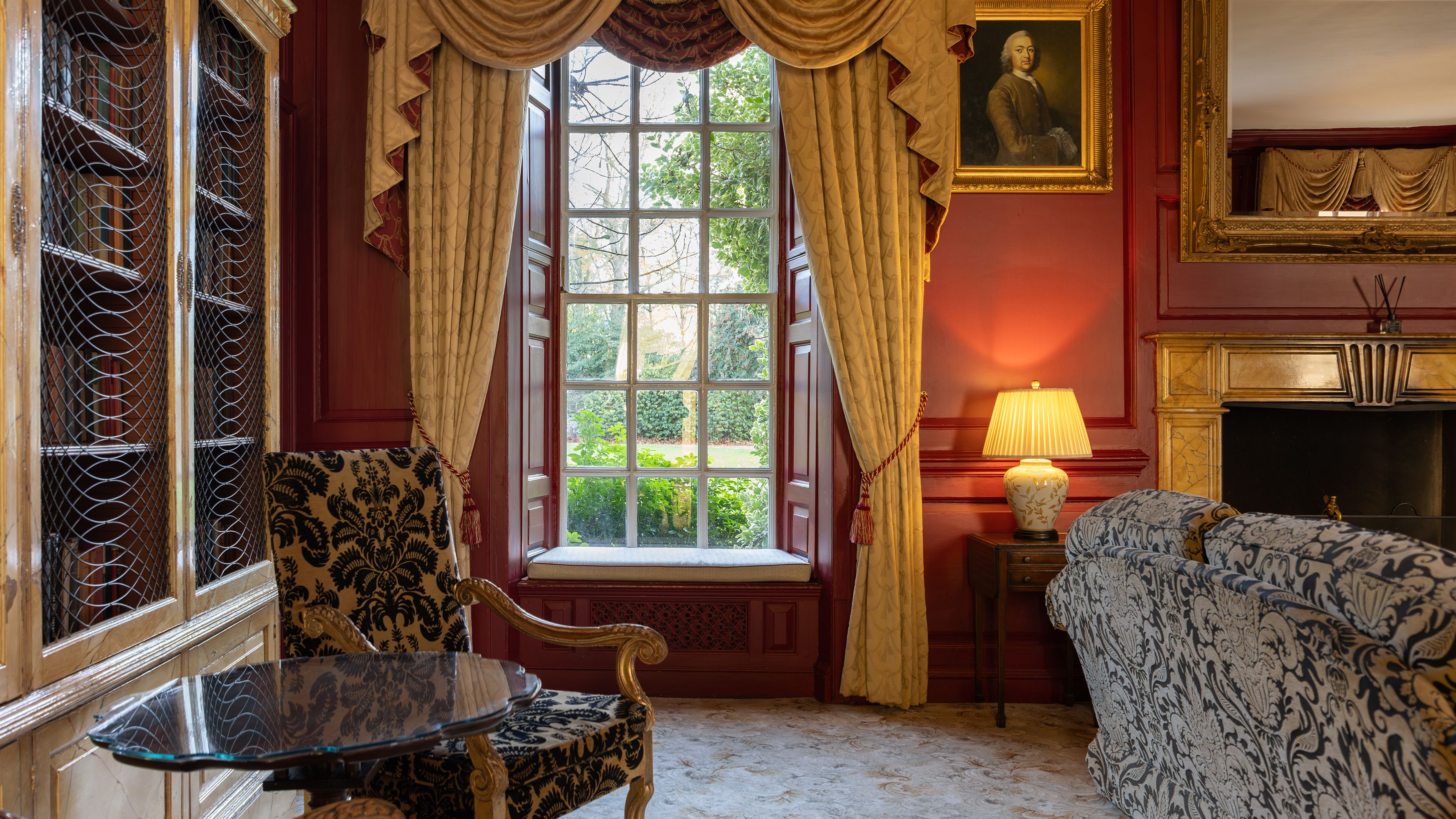 Elegant traditional living room with ornate furniture, large window, red walls, and classic decor.