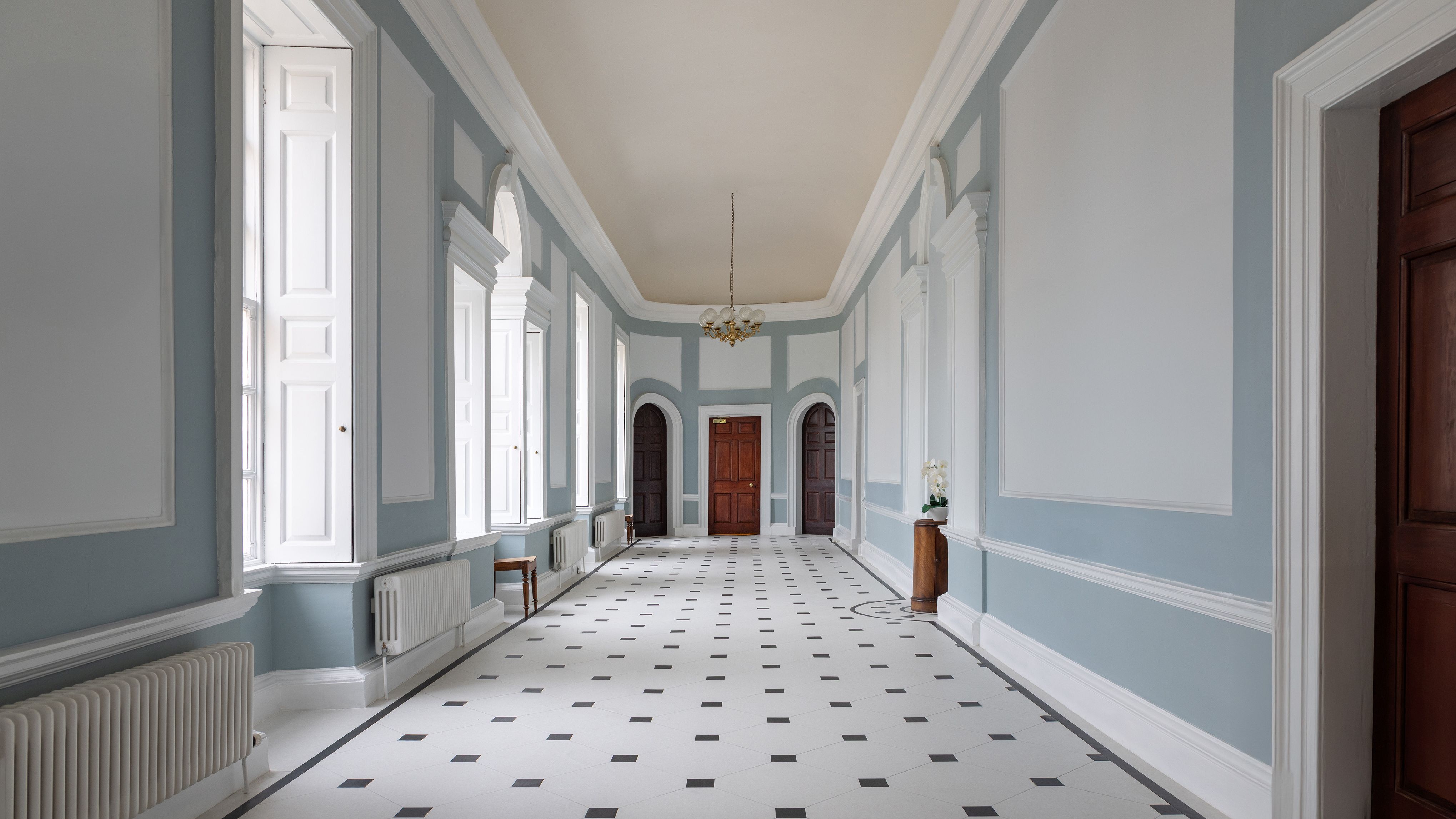 Elegant, spacious hallway with light blue walls, white paneling, and a patterned tile floor.