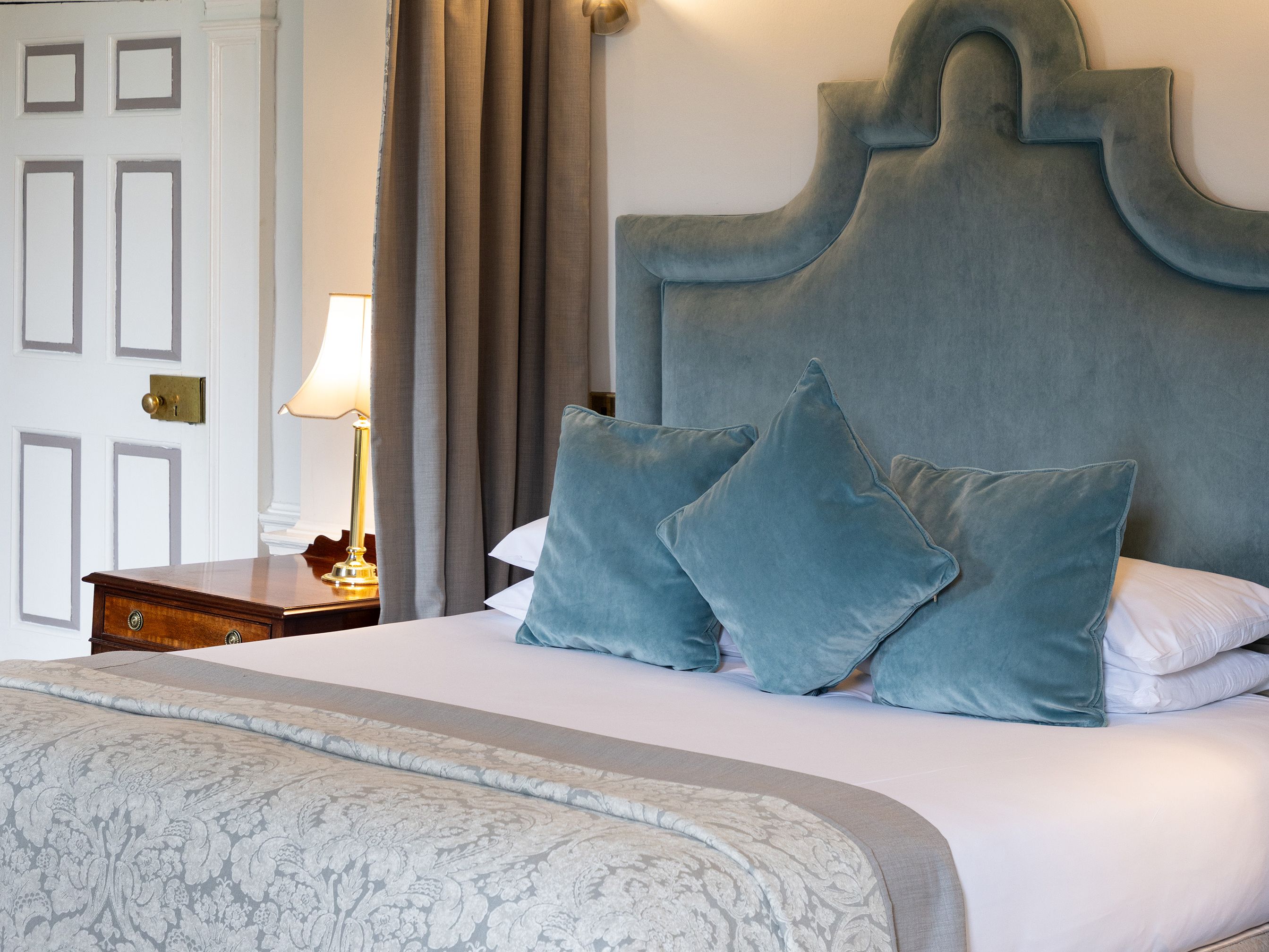 Elegant hotel bedroom with ornate canopy, blue headboard, and decorative pillows