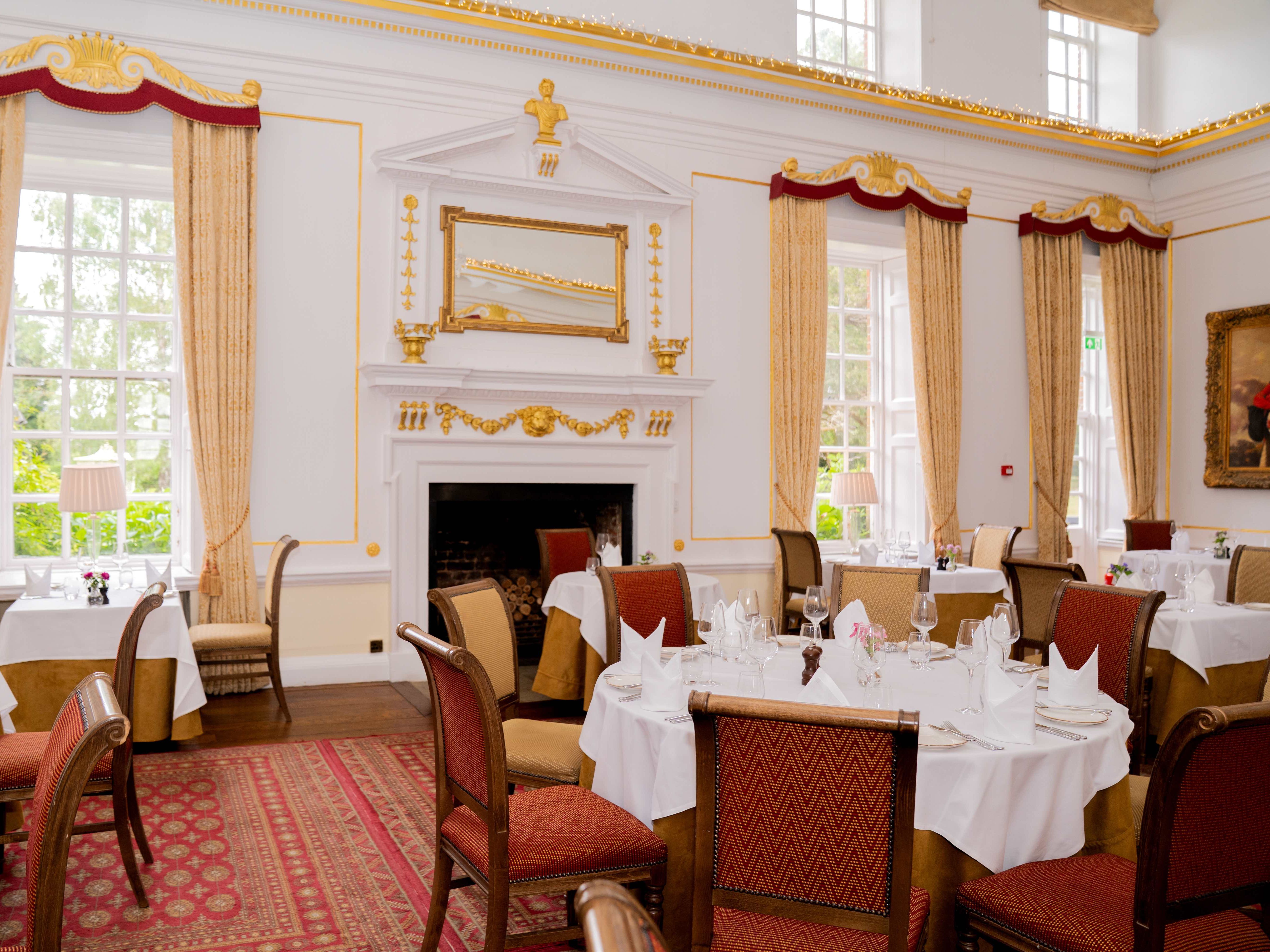 Elegant dining room with classic decor, round tables with white tablecloths and red cushioned chairs.