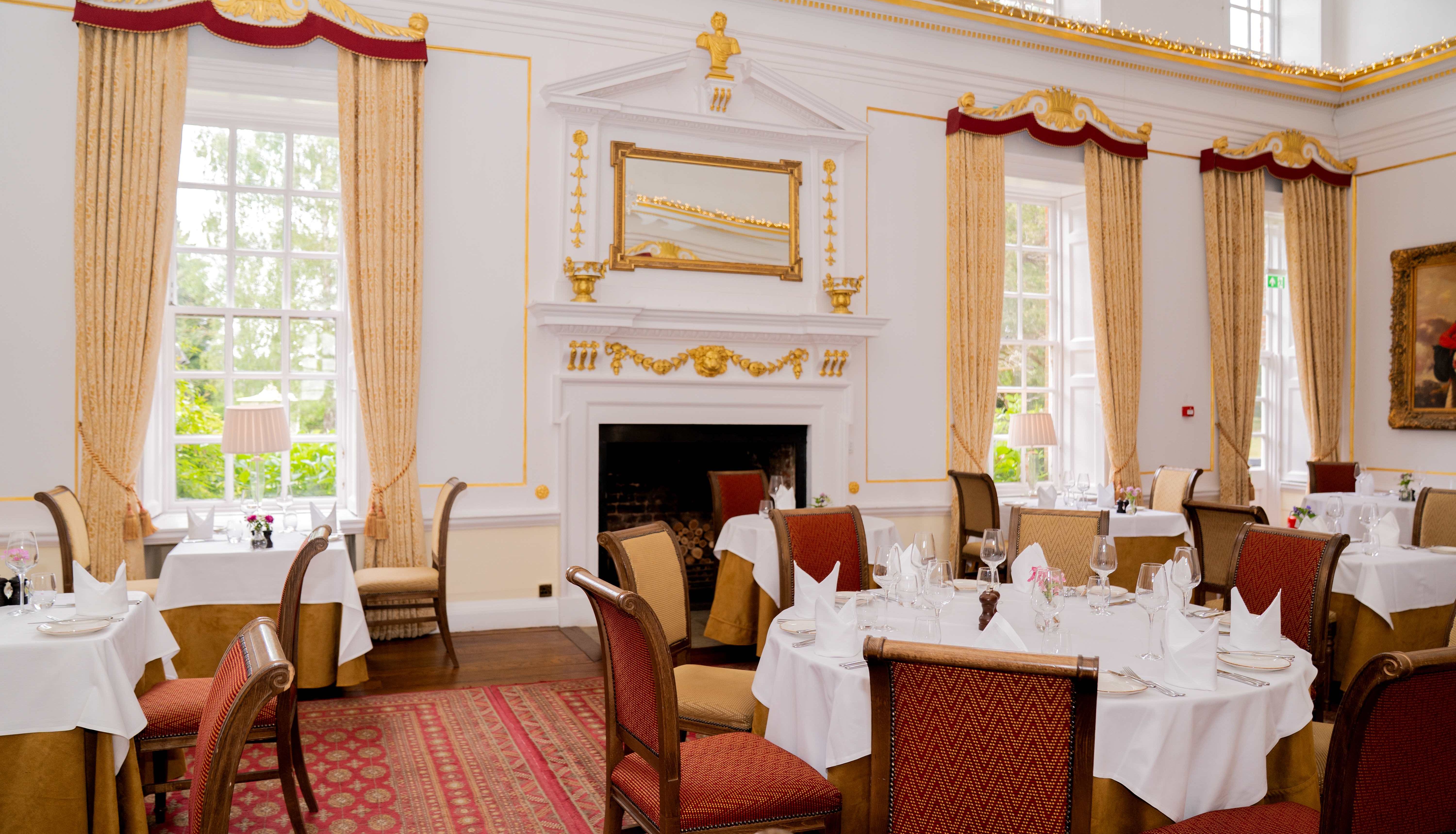 Elegant dining room with classic decor, round tables with white tablecloths and red cushioned chairs.