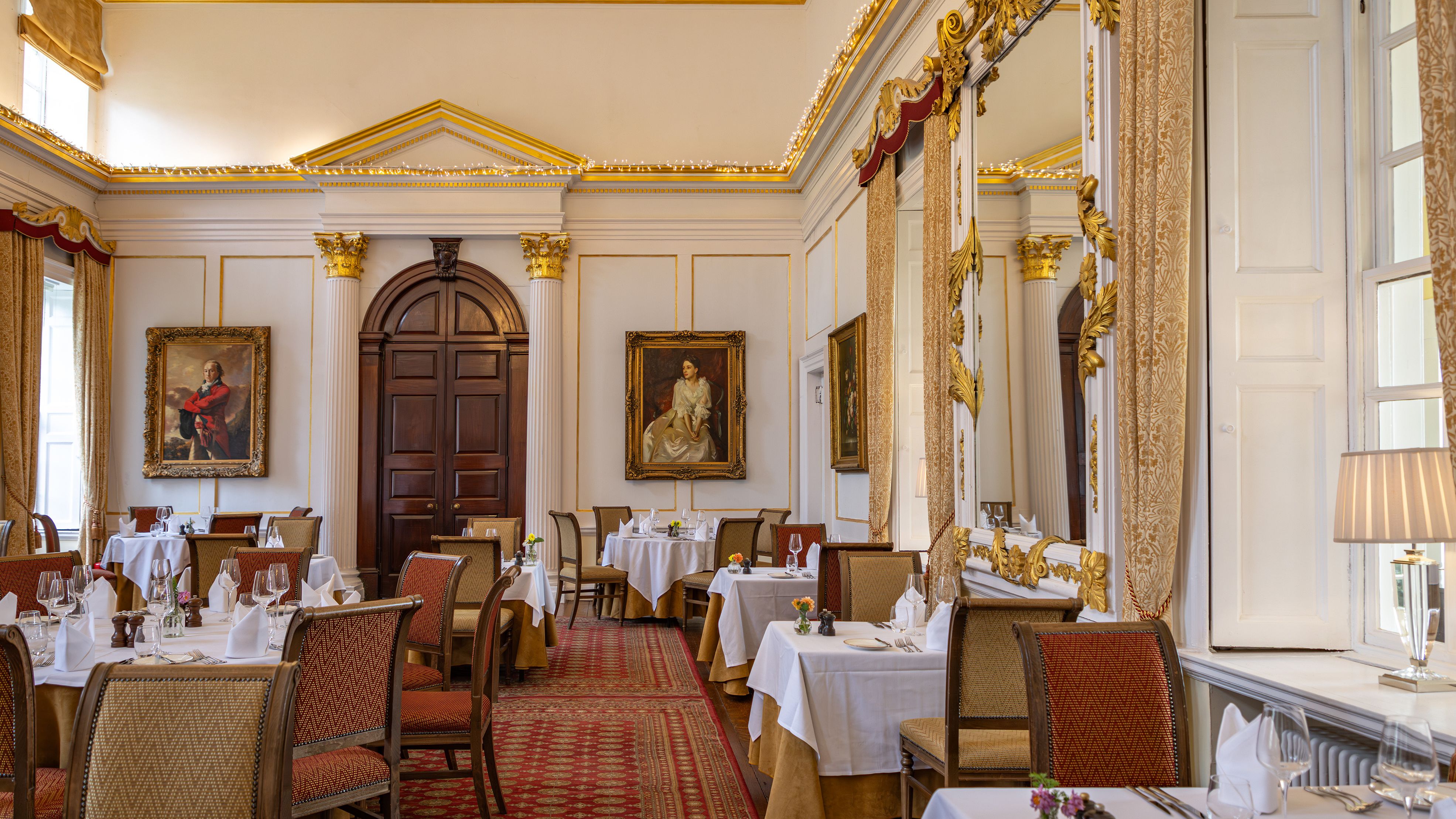 Elegant classical dining room with gold accents, large mirrors, and portrait paintings.