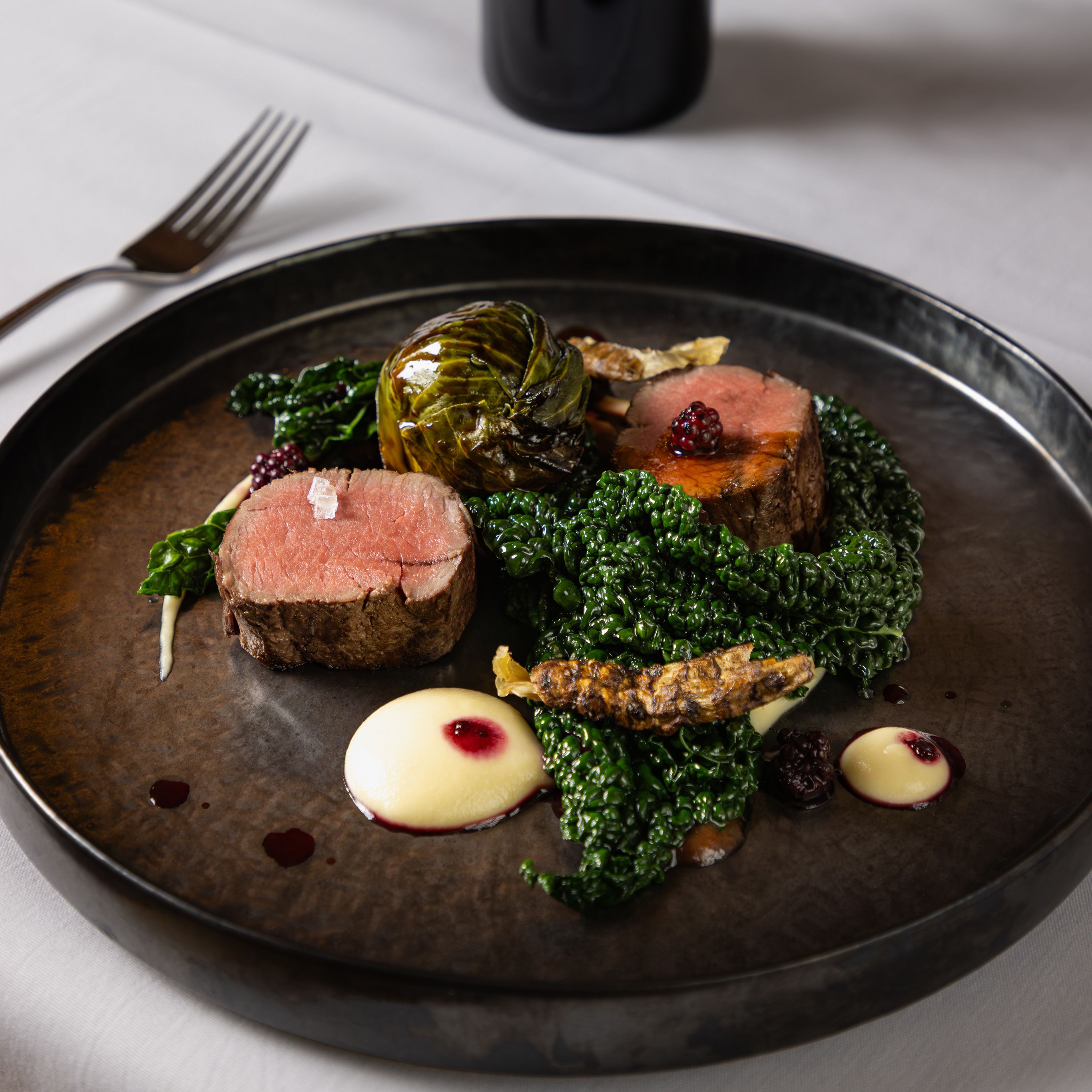 Gourmet plated beef dish with greens and sauce, served with a bottle of red wine