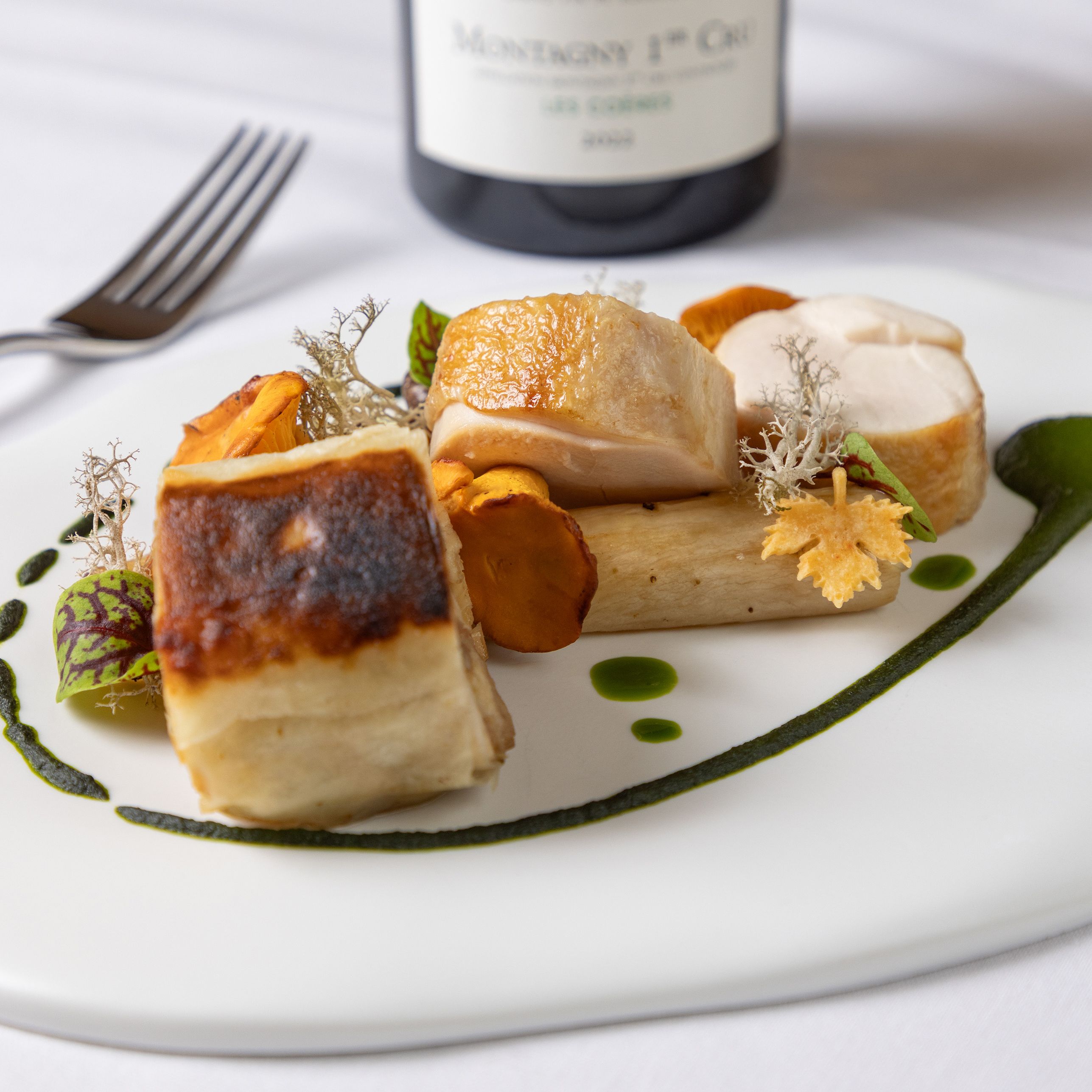 Gourmet plated chicken dish with green sauce, mushrooms, and garnishes on a white plate.