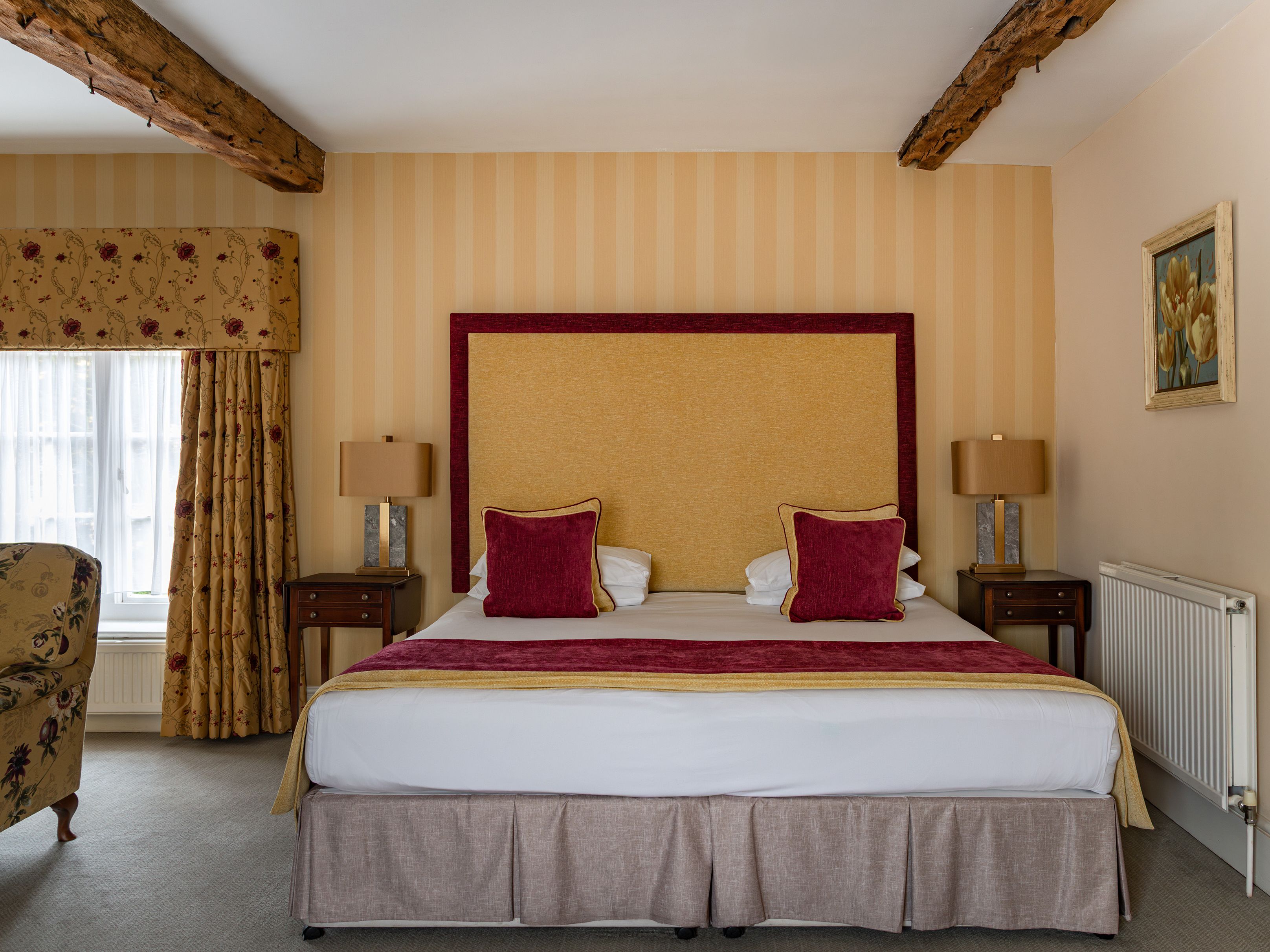Elegant bedroom with a large bed, wooden beams, and floral curtains.