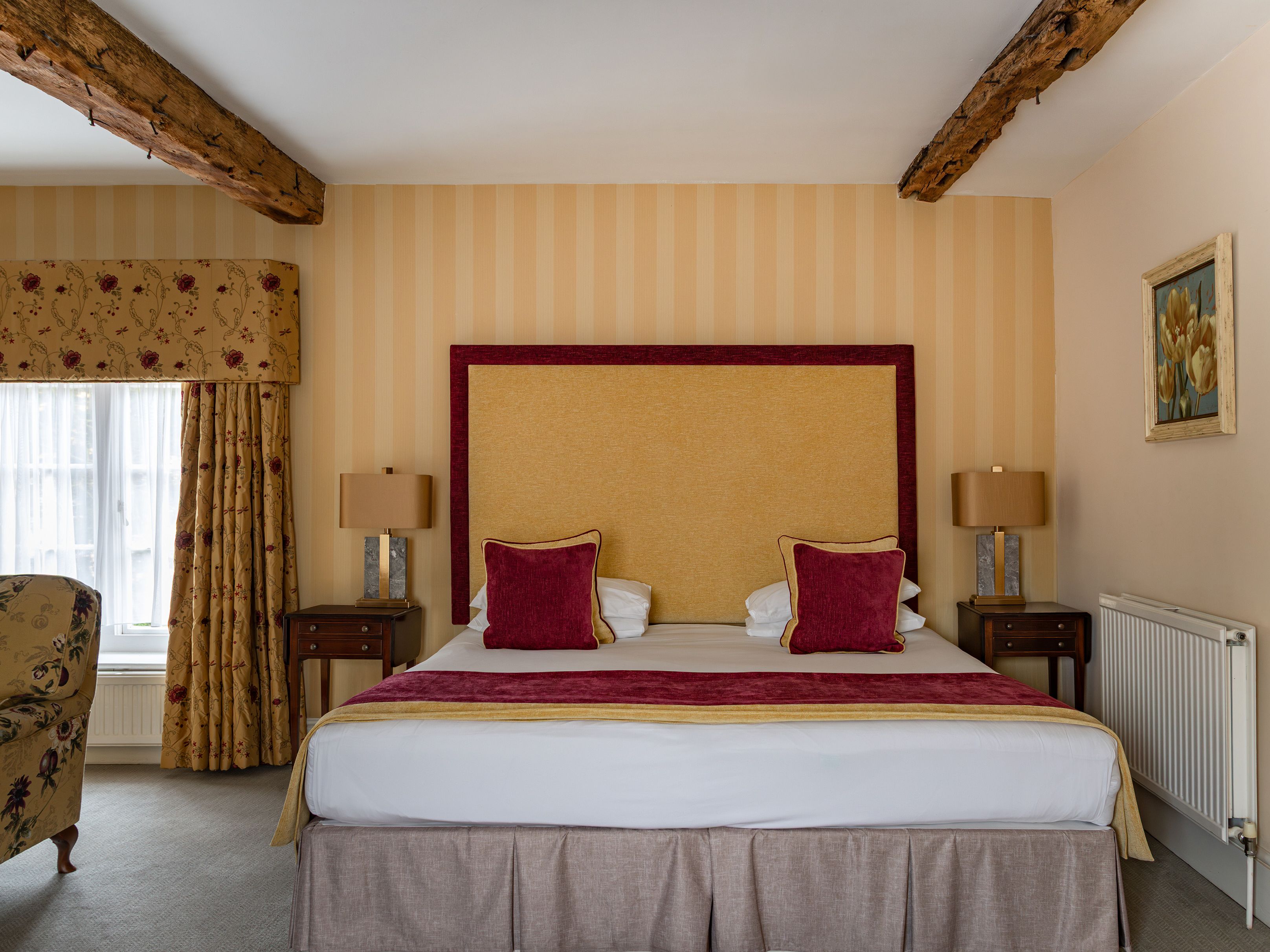Elegant bedroom with a large bed, wooden beams, and floral curtains.