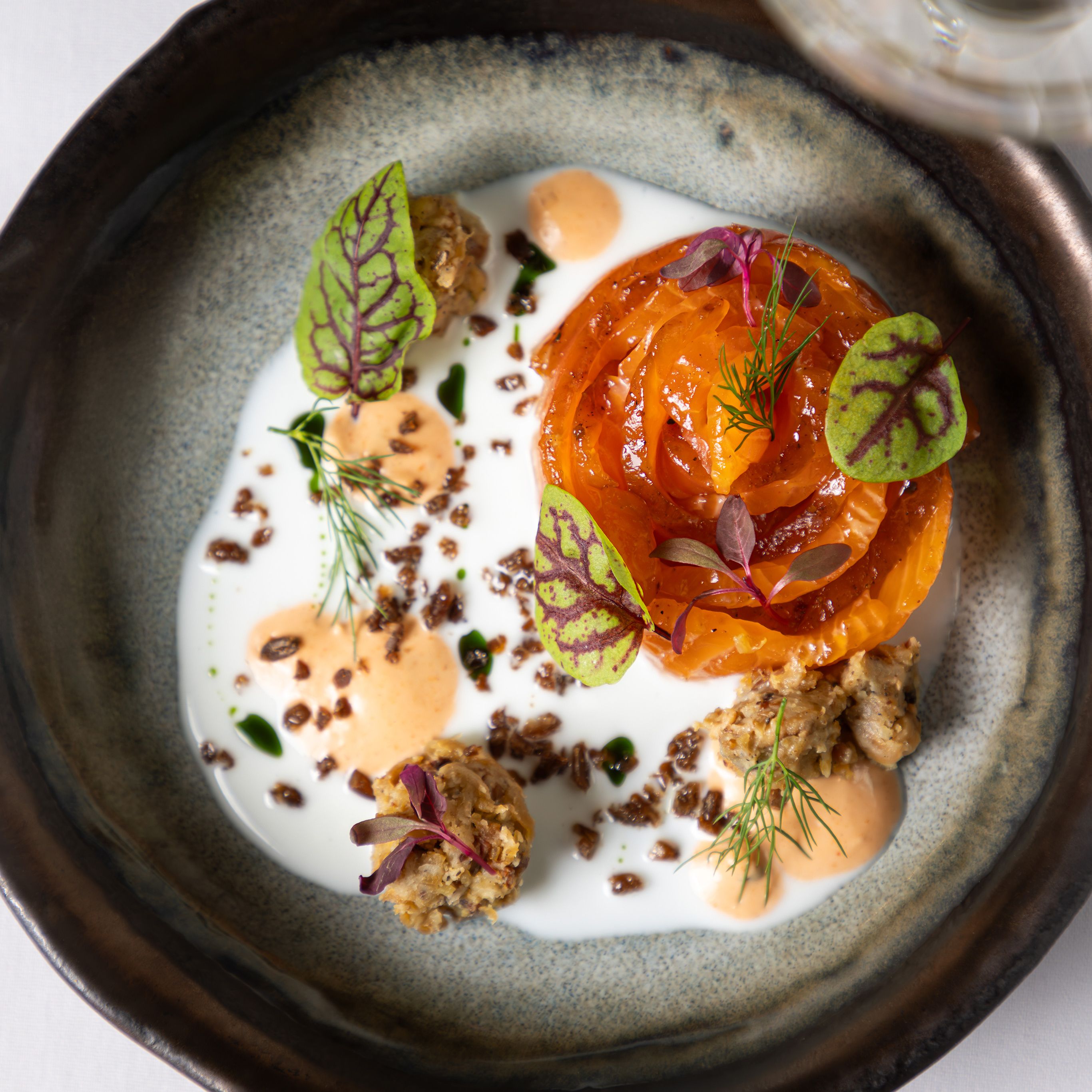 Gourmet plated dish with tomato, sauce, microgreens, and a glass of white wine