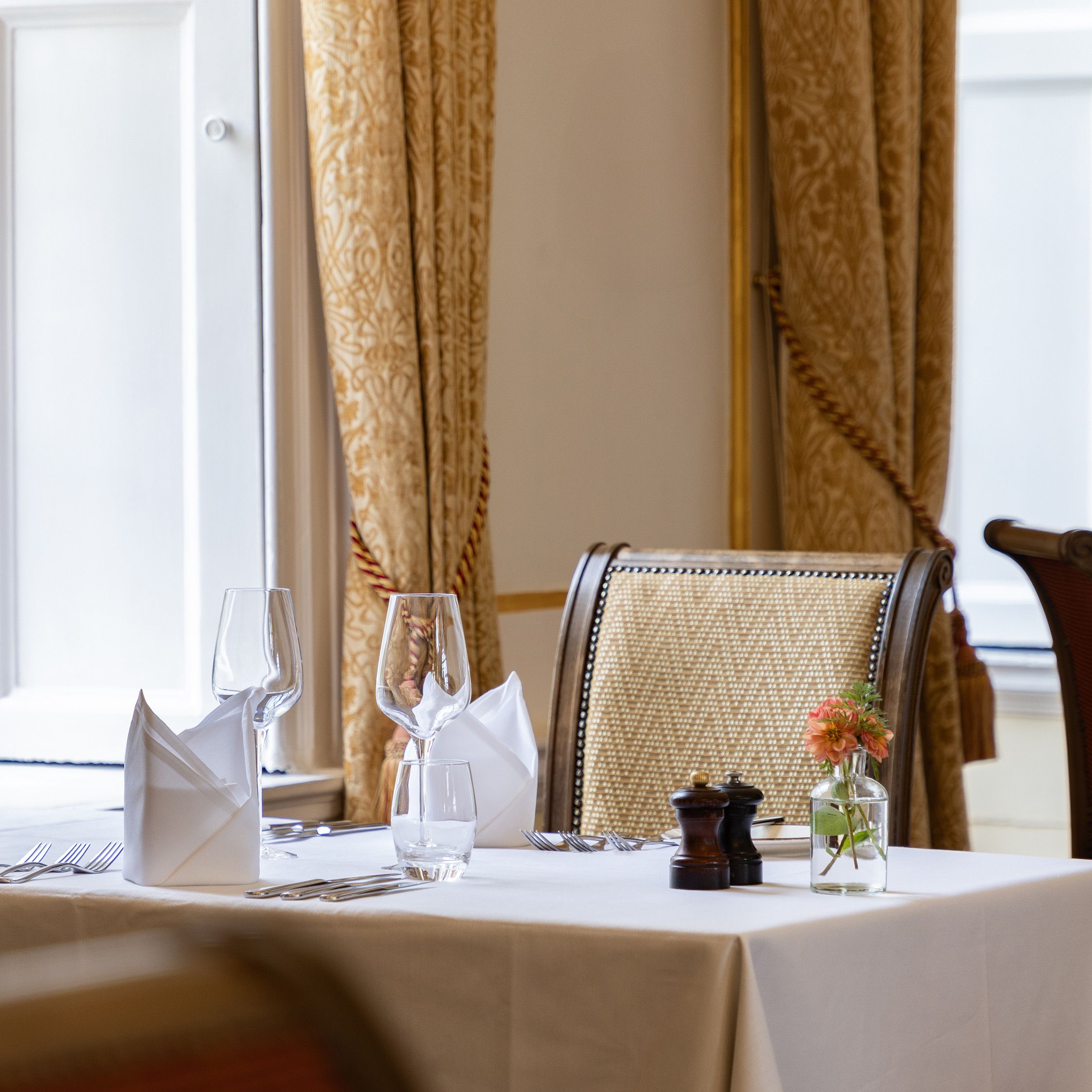 Elegant restaurant table set for two with white tablecloth, napkins, wine glasses, and a small flower vase