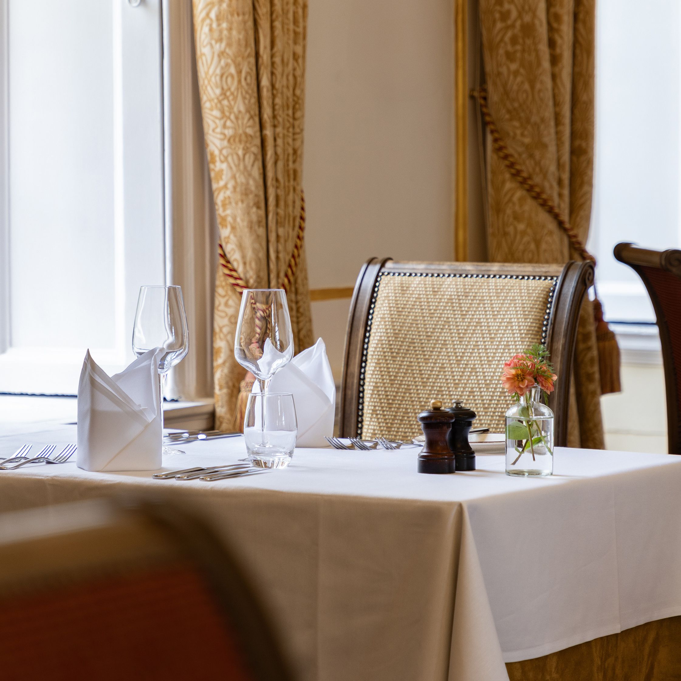 Elegant restaurant table set for two with white tablecloth, napkins, wine glasses, and a small flower vase