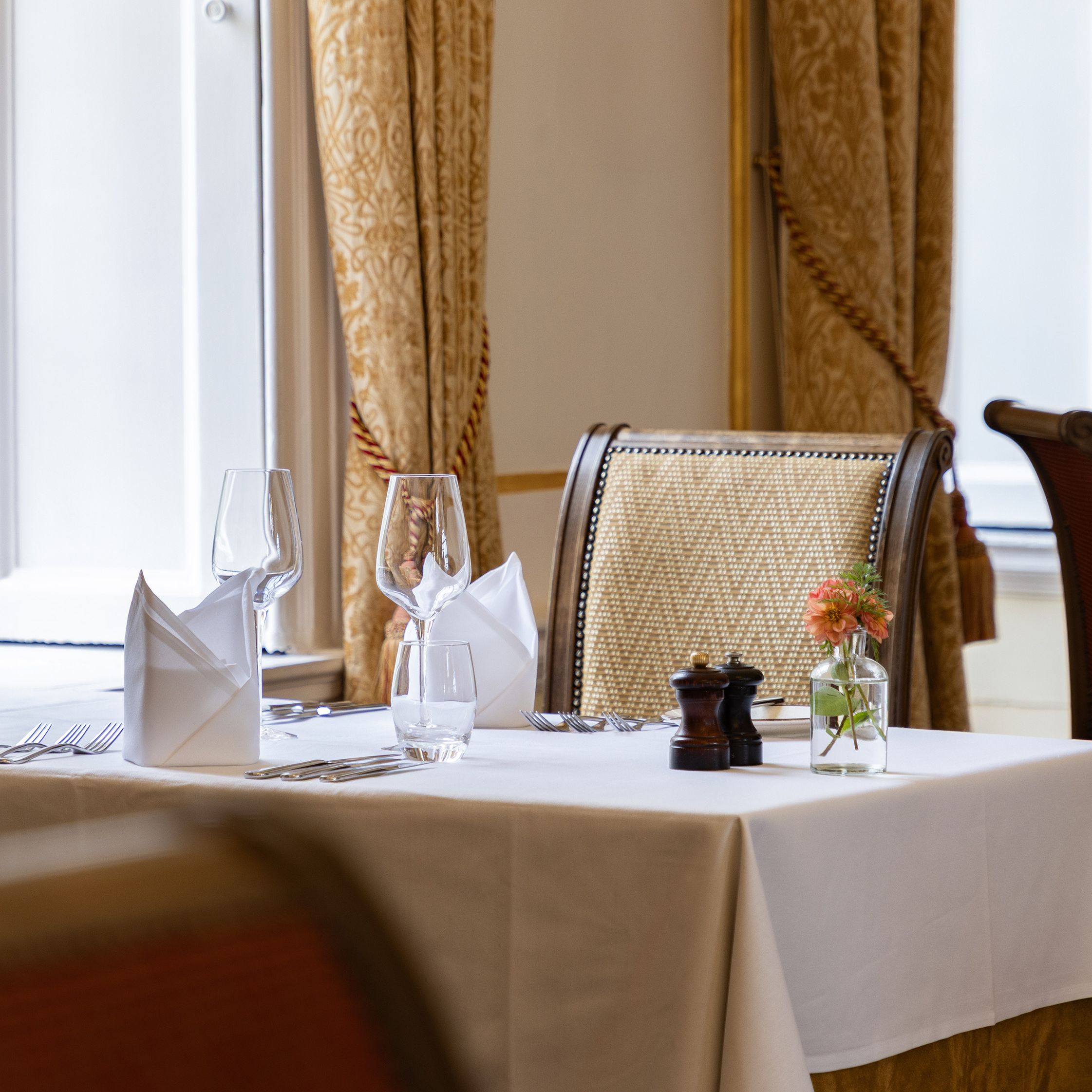 Elegant restaurant table set for two with white tablecloth, napkins, wine glasses, and a small flower vase