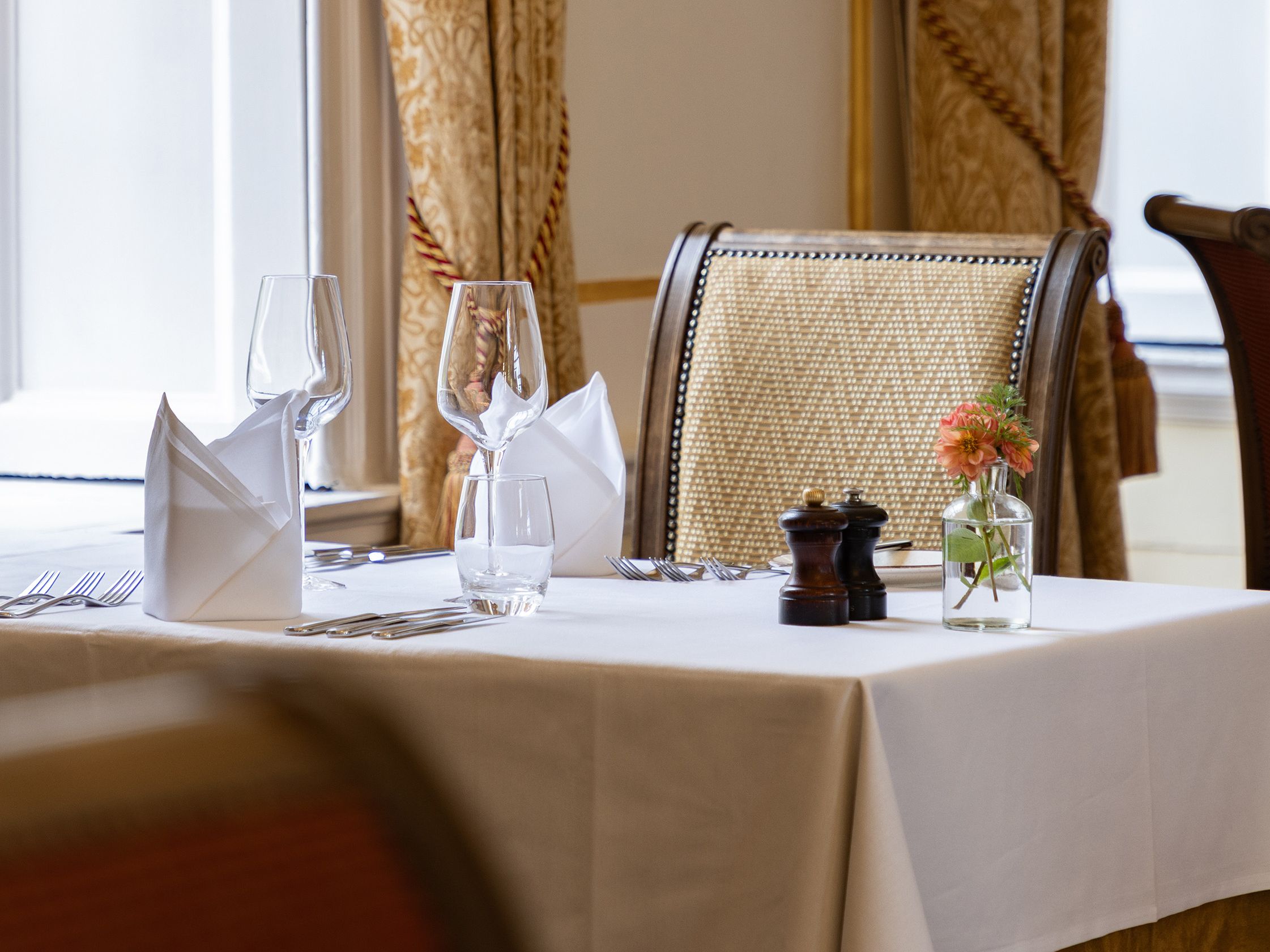 Elegant restaurant table set for two with white tablecloth, napkins, wine glasses, and a small flower vase