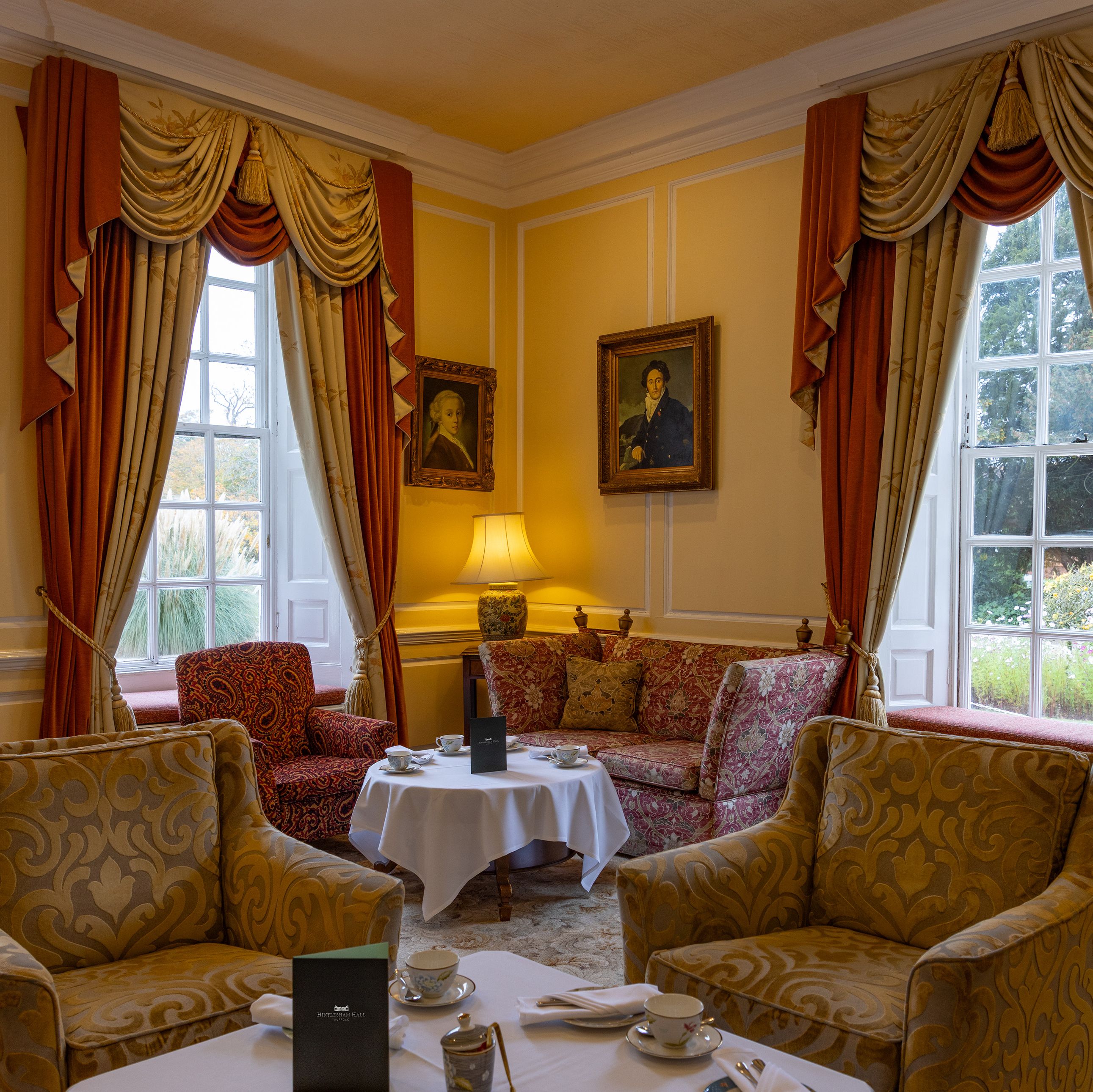 Elegant sitting room with patterned armchairs, draped curtains, and a tea setting on round tables.