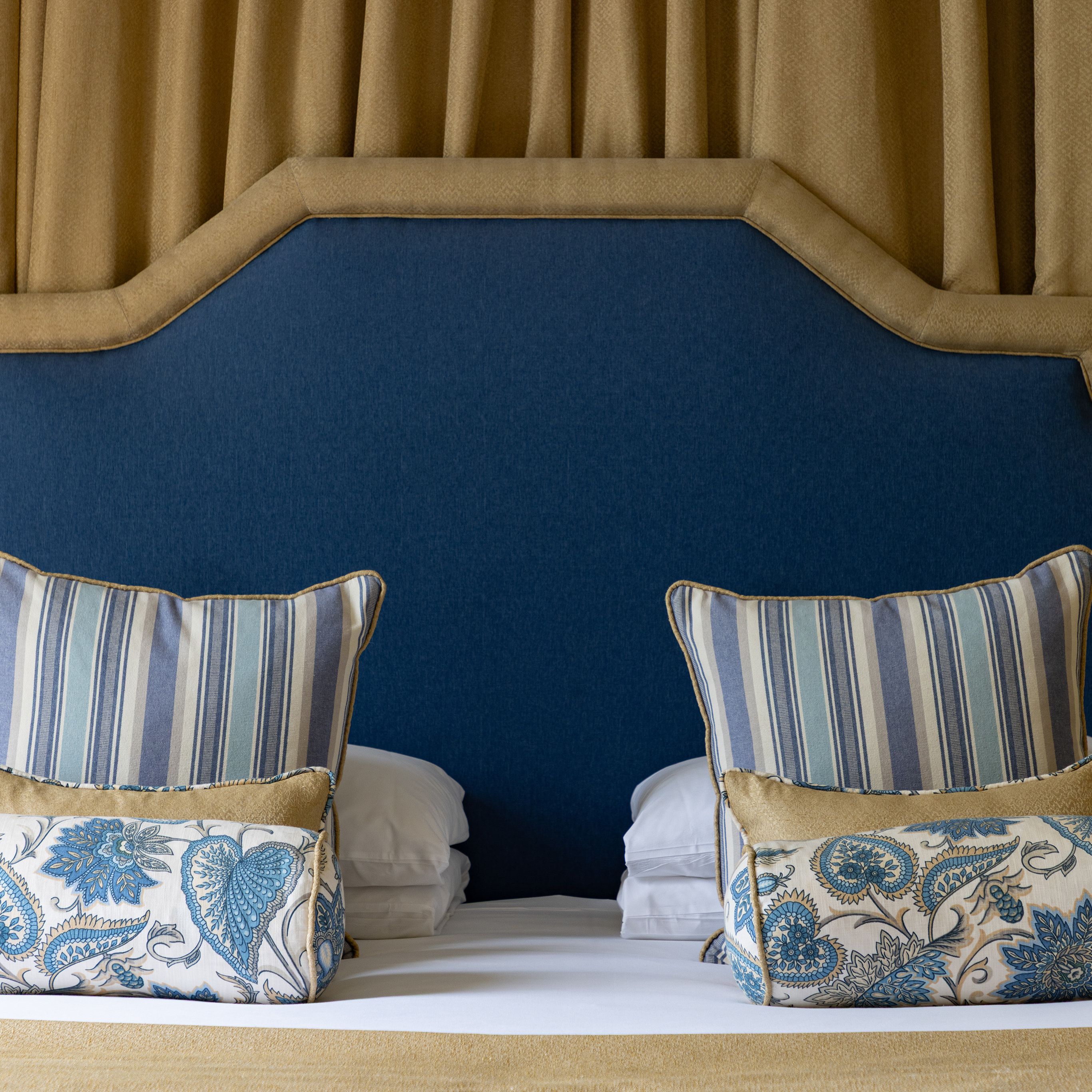 Elegant bed with blue headboard, striped and patterned pillows, and gold drapes