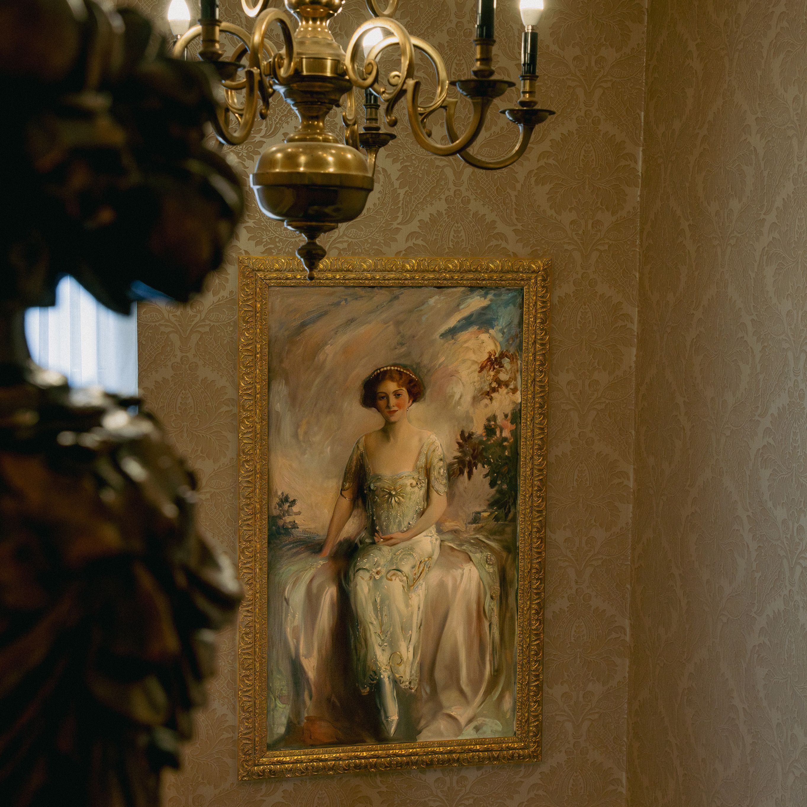 Elegant chandelier and framed portrait of a seated woman in a classical interior