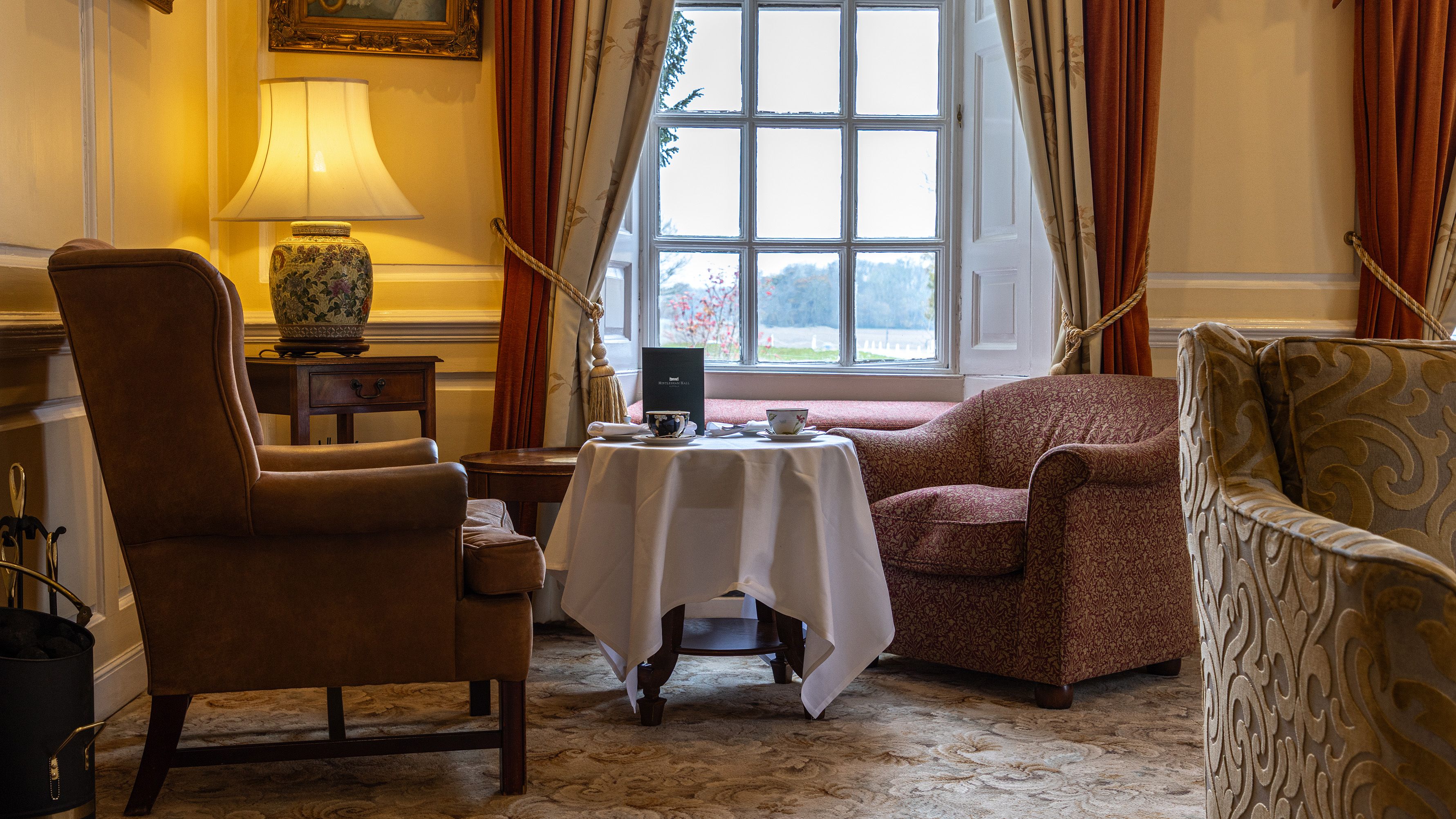 Cozy sitting area with armchairs, a table set for tea, and a window with elegant curtains.