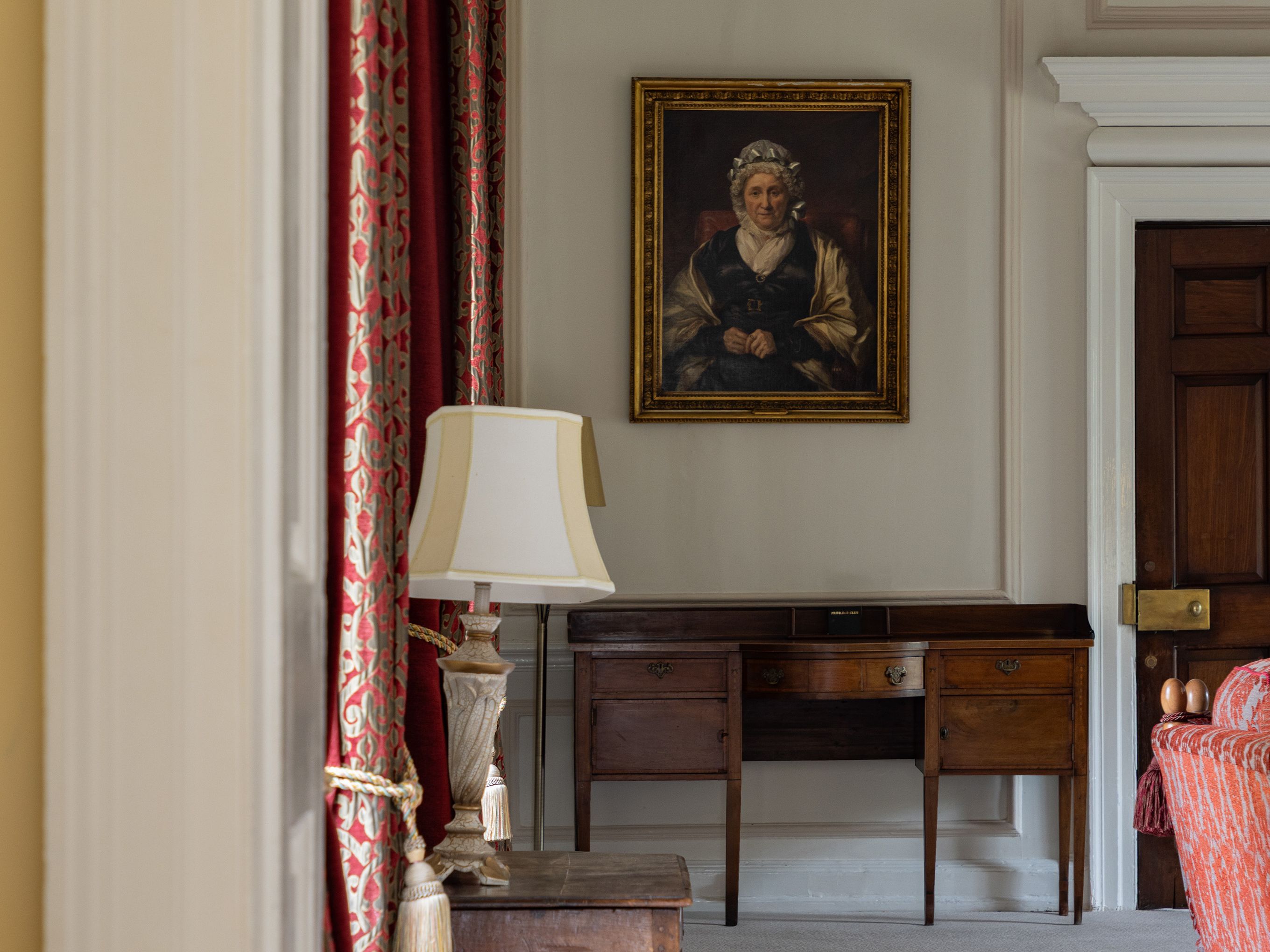 Traditional room with a portrait on the wall, wooden furniture, and red patterned curtains.