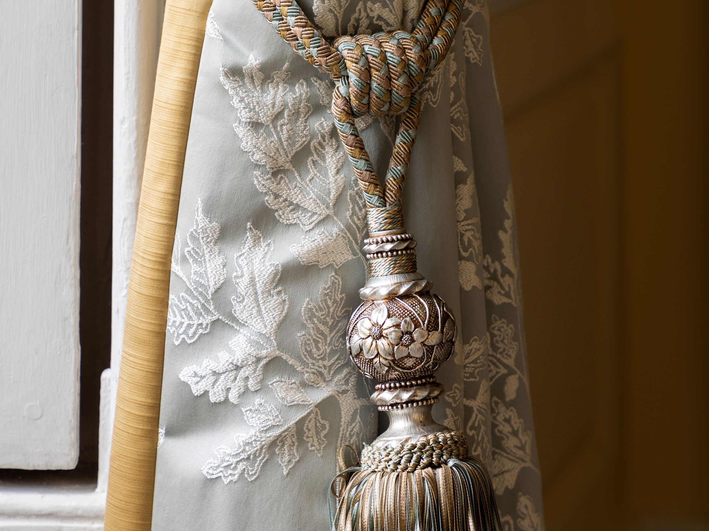 Ornate curtain tieback with tassel on embroidered drapery