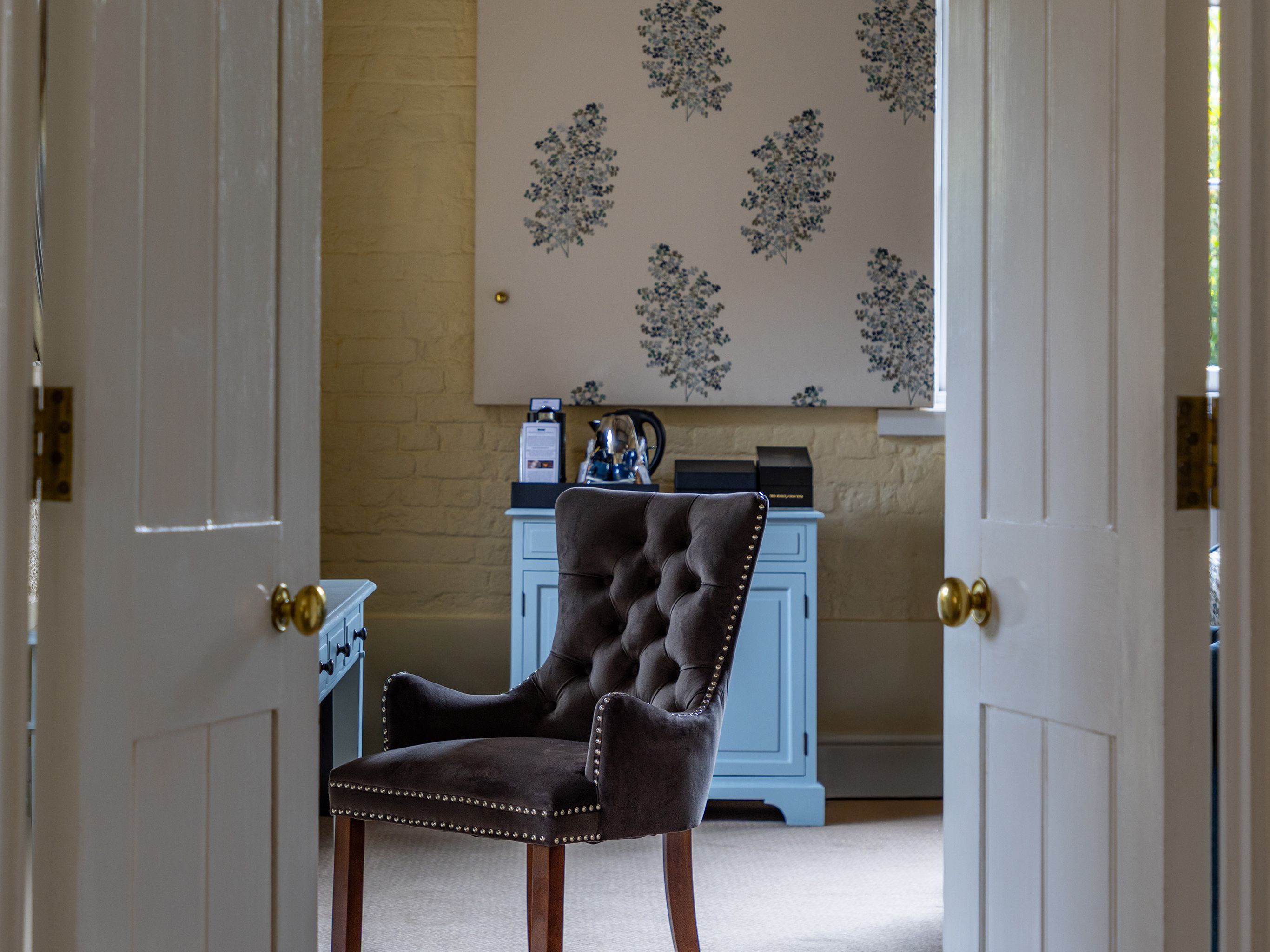A cozy home office with a velvet tufted chair, painted blue furniture, and floral wall decor.