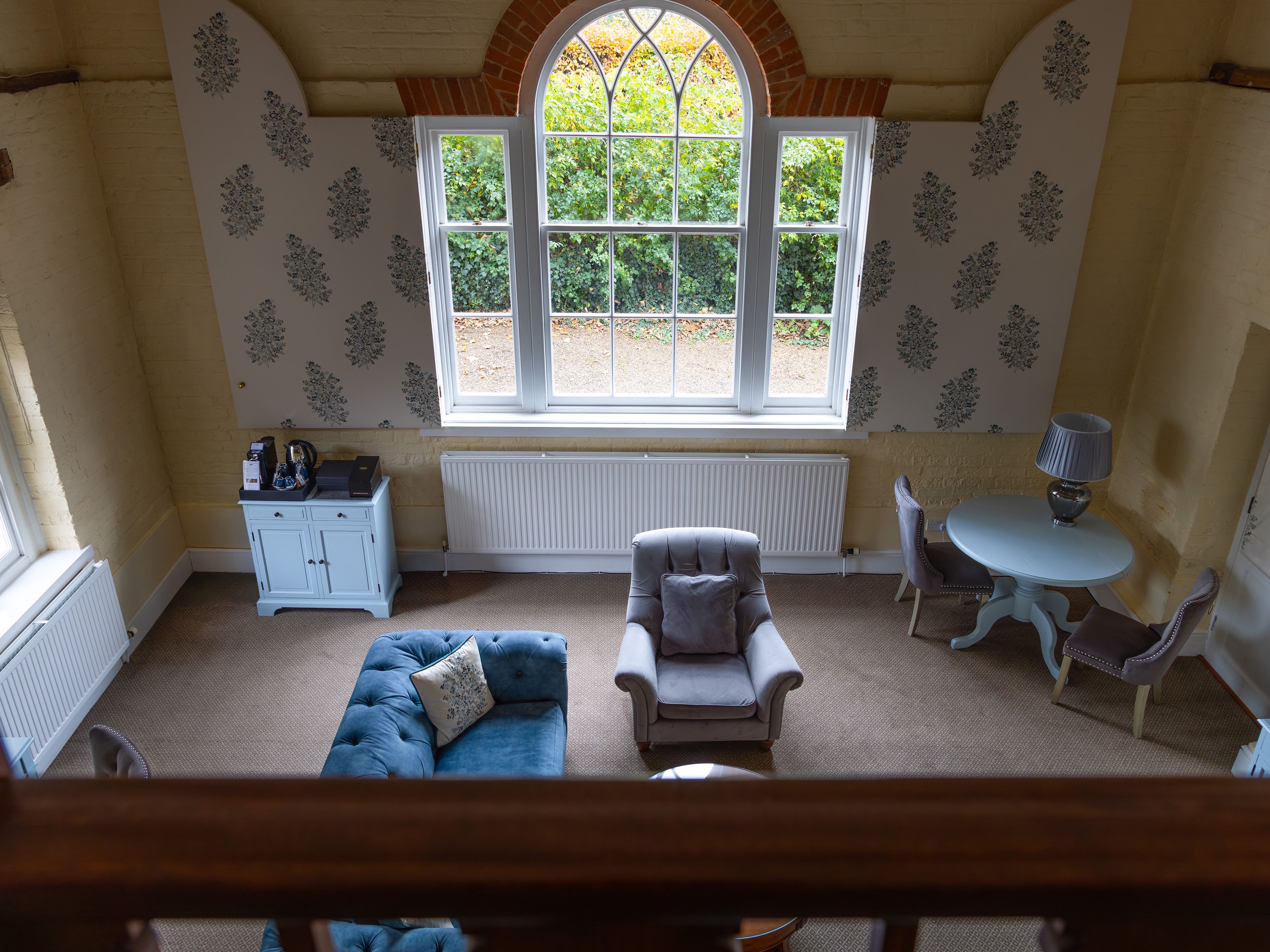 A view of a cozy, stylish living room with a large arched window, pastel furniture, and neutral decor.
