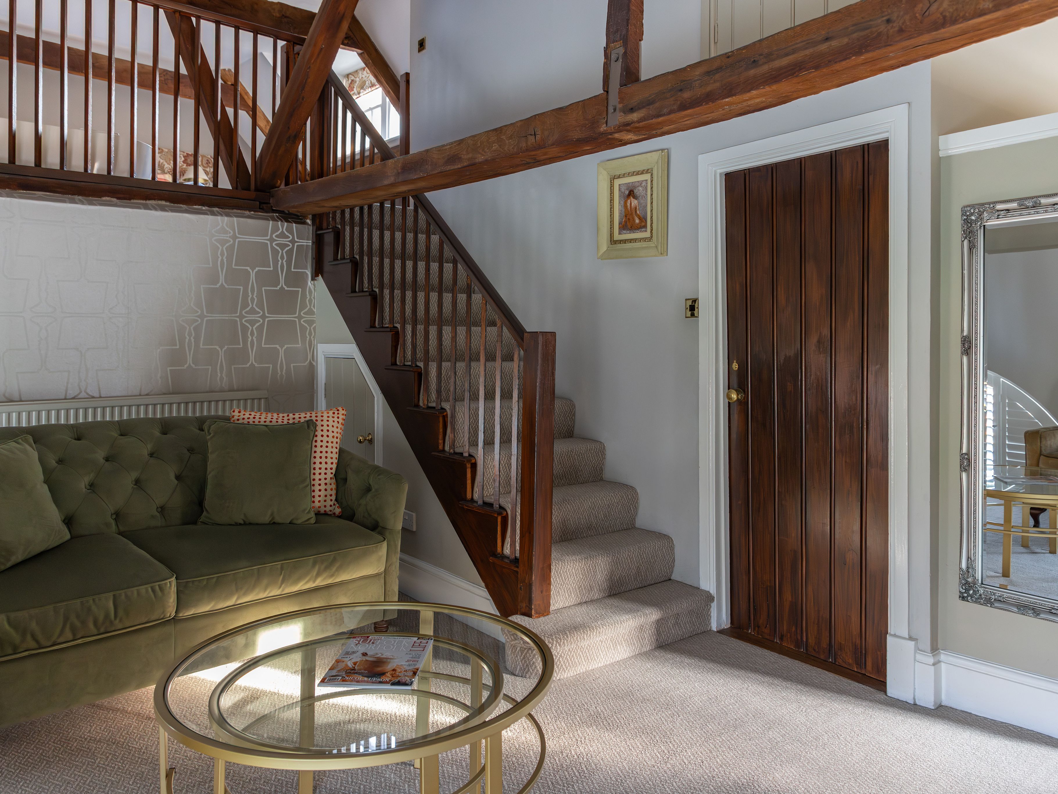 Cozy living room with green sofa, wooden staircase, glass coffee table, and wooden door.