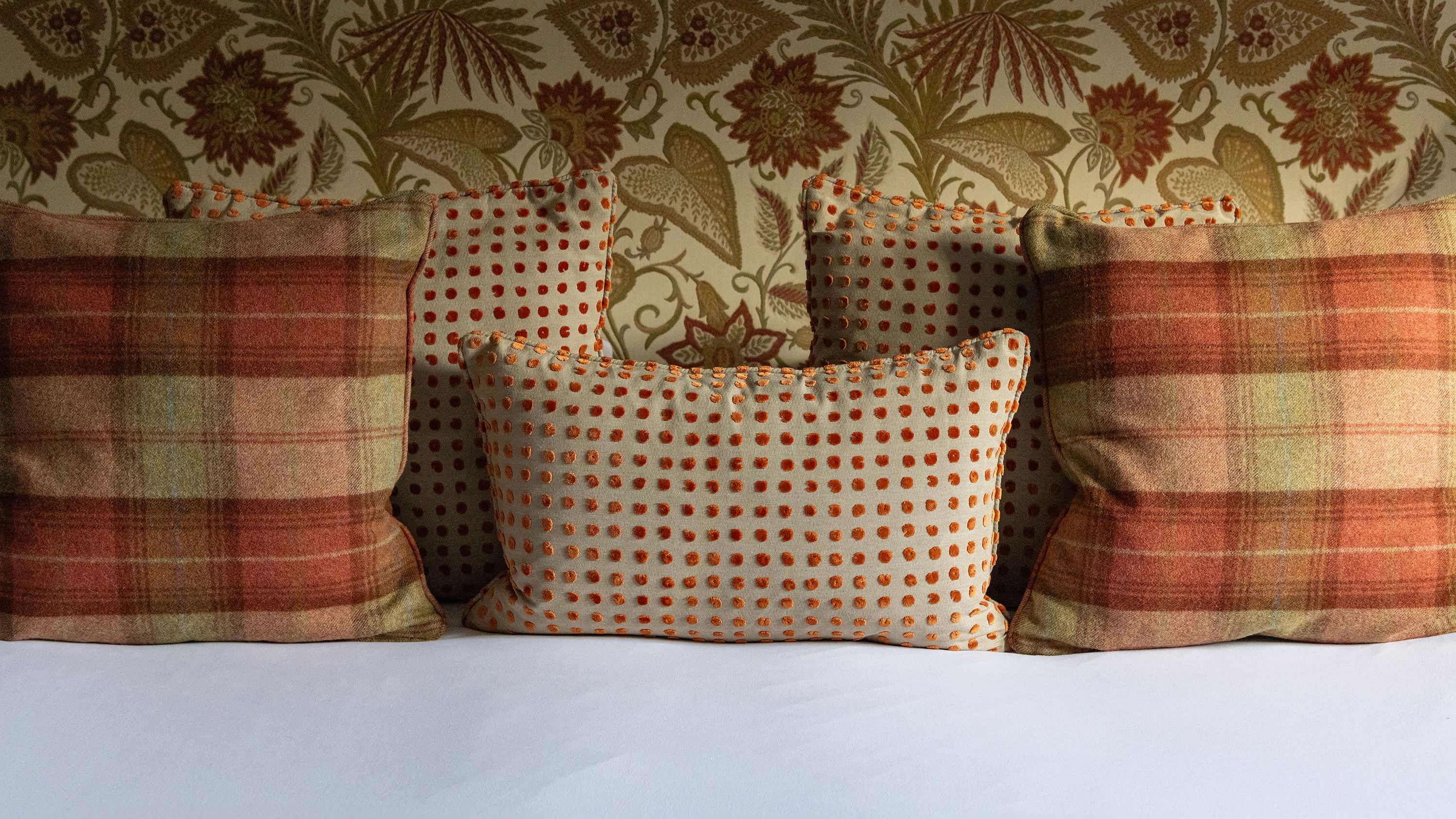 Decorative pillows with plaid and polka dot patterns against a floral wallpaper background