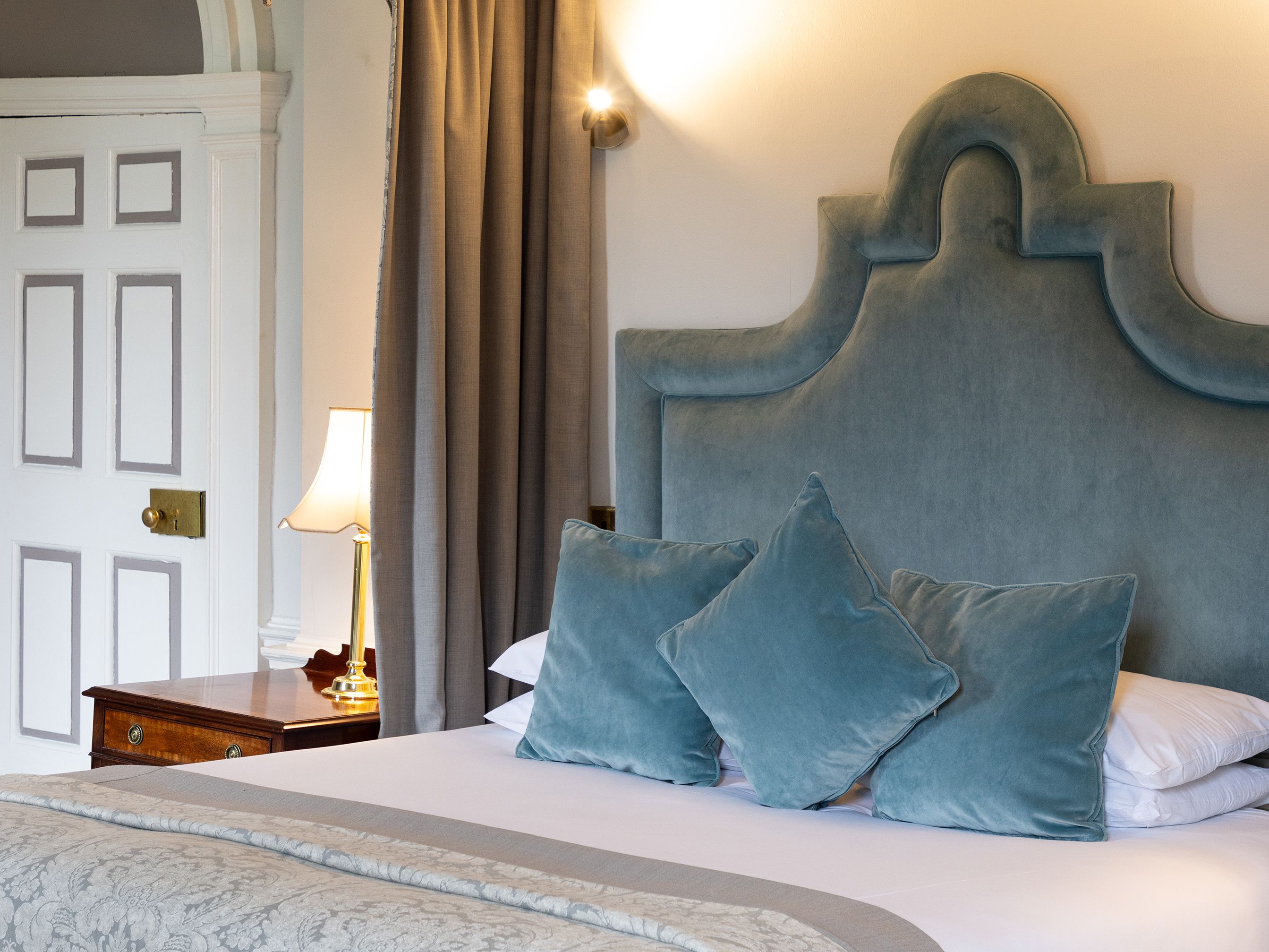 Luxurious bed with blue velvet headboard, matching blue pillows, and ornate canopy in an elegant bedroom.