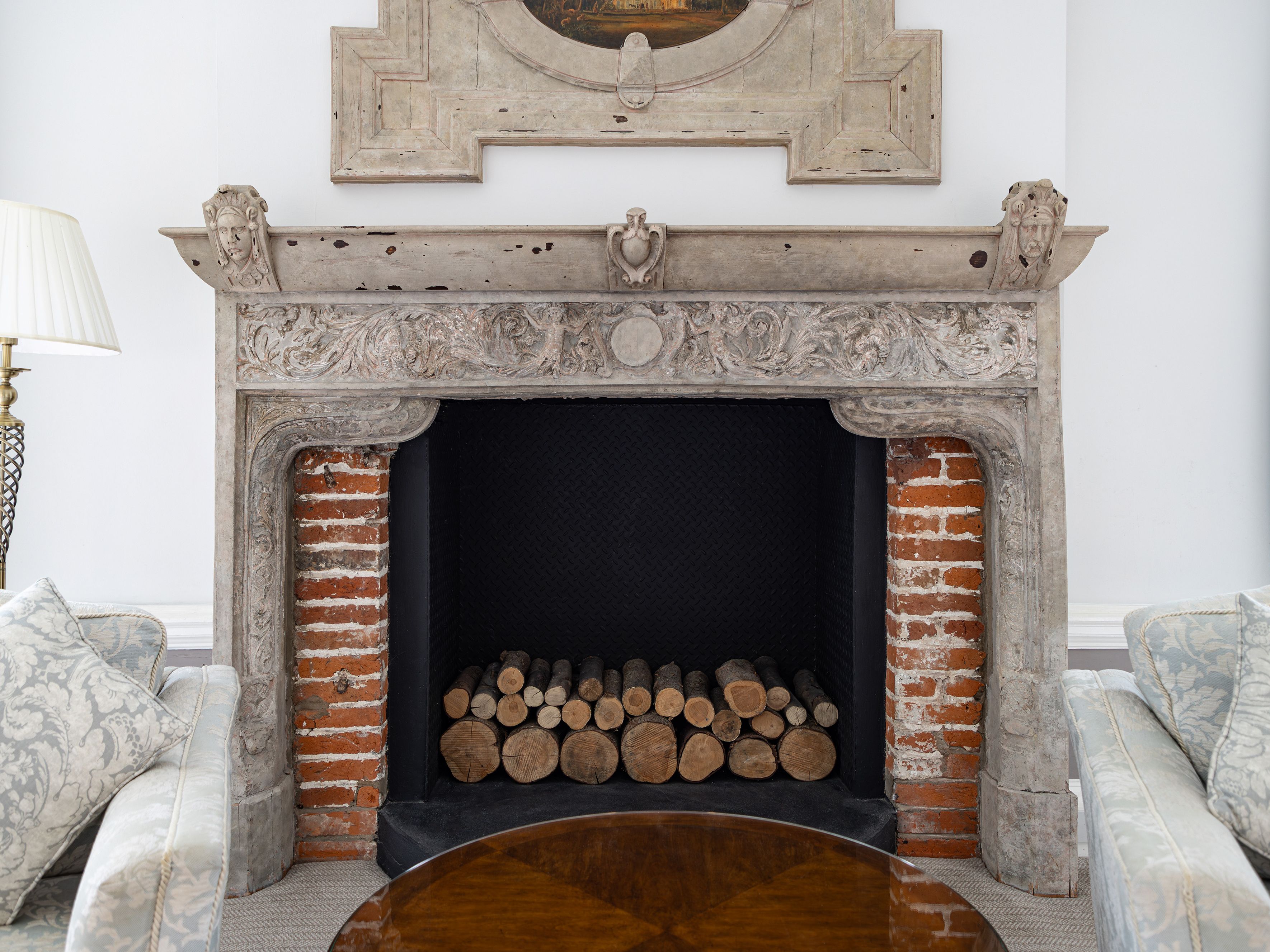 Antique stone fireplace with ornate carvings and stacked firewood inside