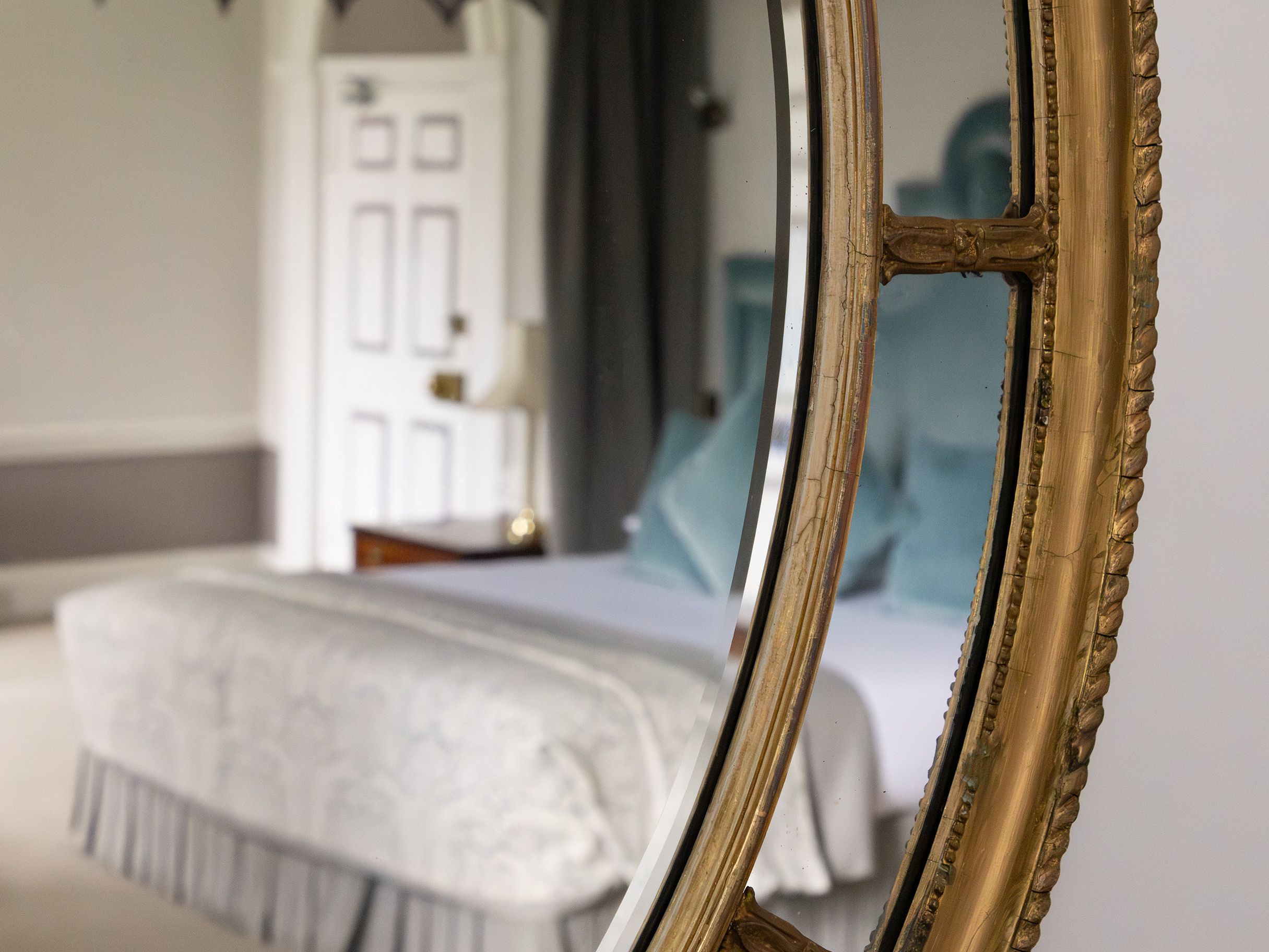 Reflection of a bedroom in a round, gold-framed mirror