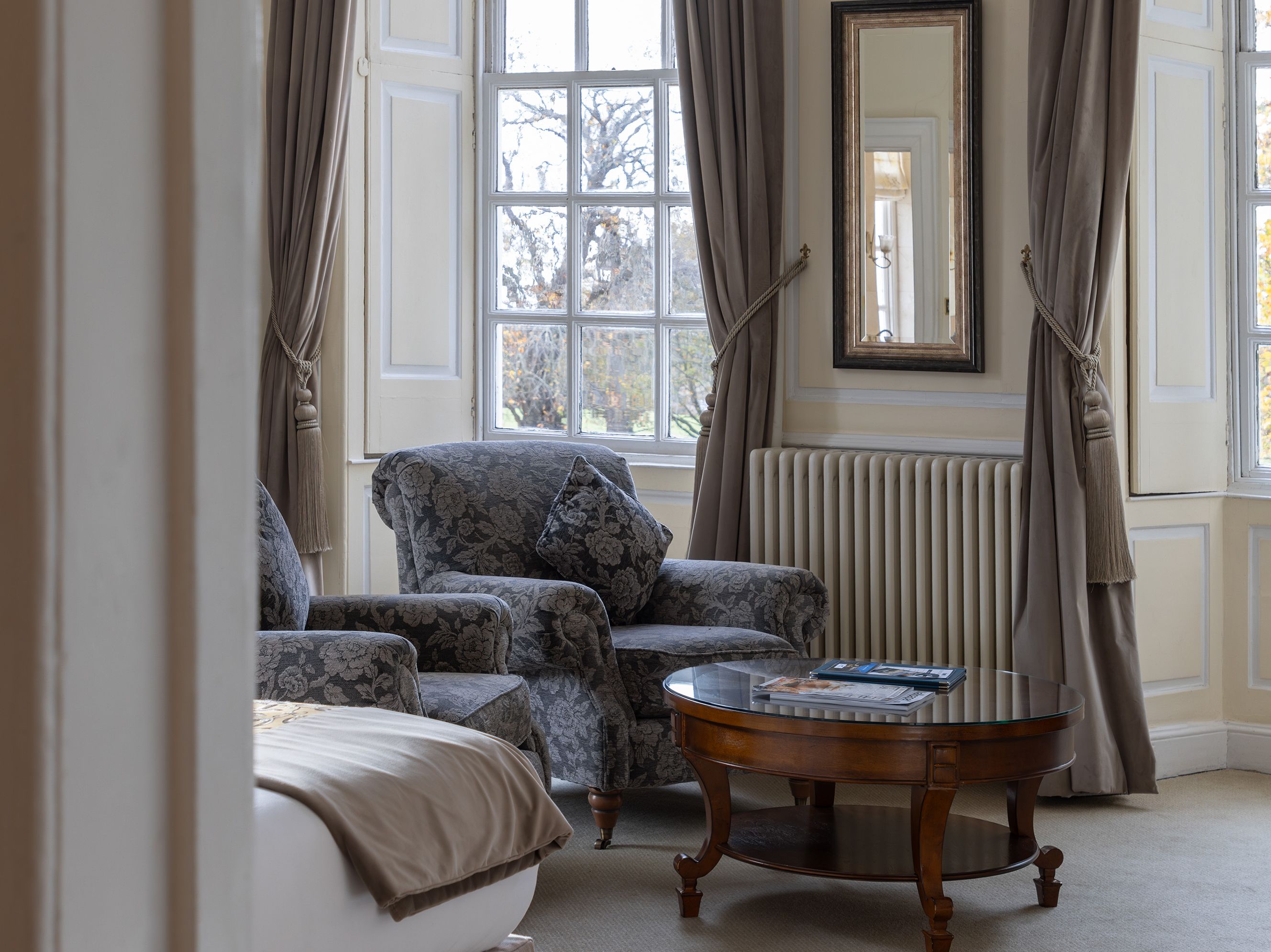 Bright, elegant sitting area in a bedroom with armchairs, a coffee table, and large windows with drapes.