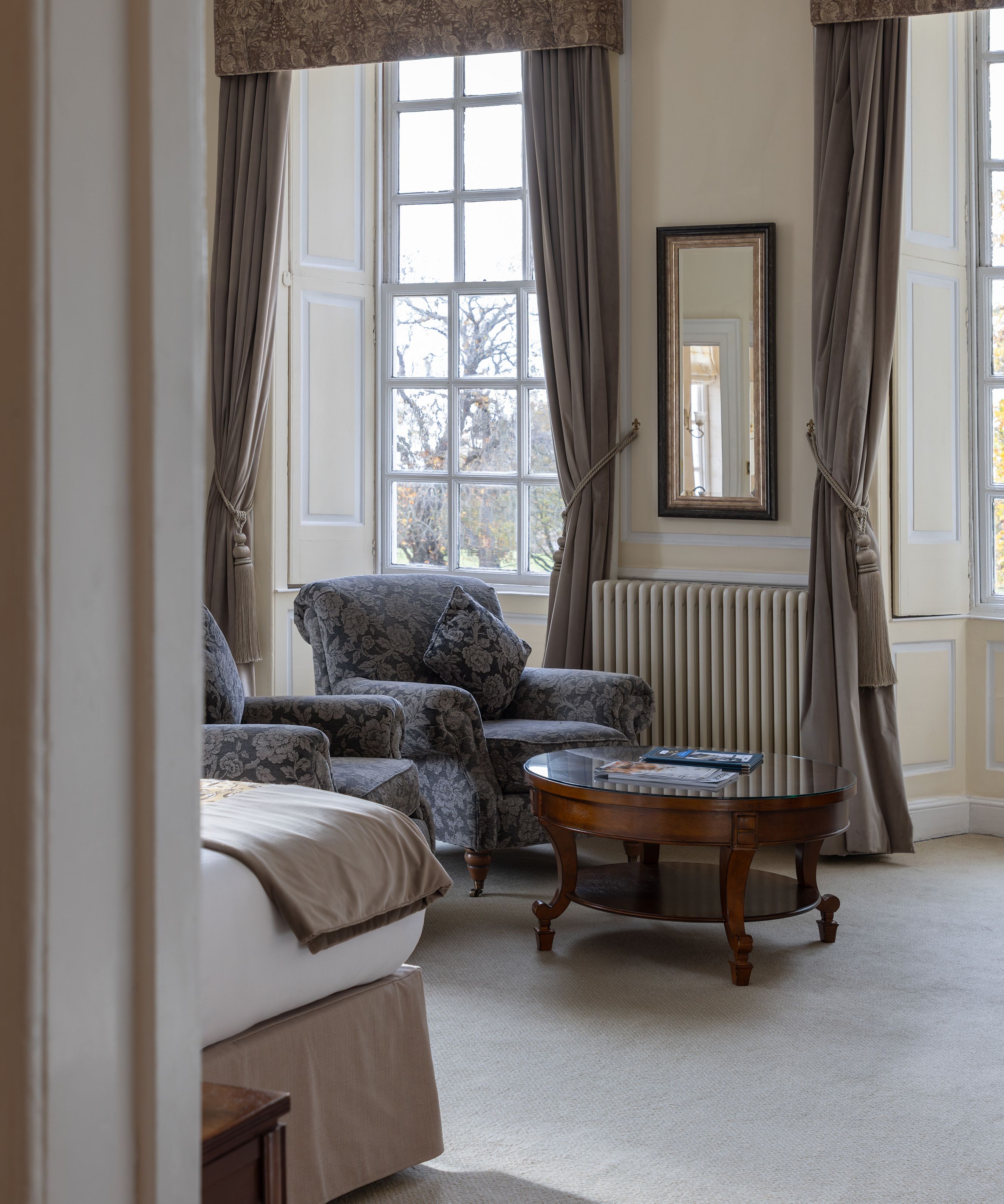 Bright, elegant sitting area in a bedroom with armchairs, a coffee table, and large windows with drapes.