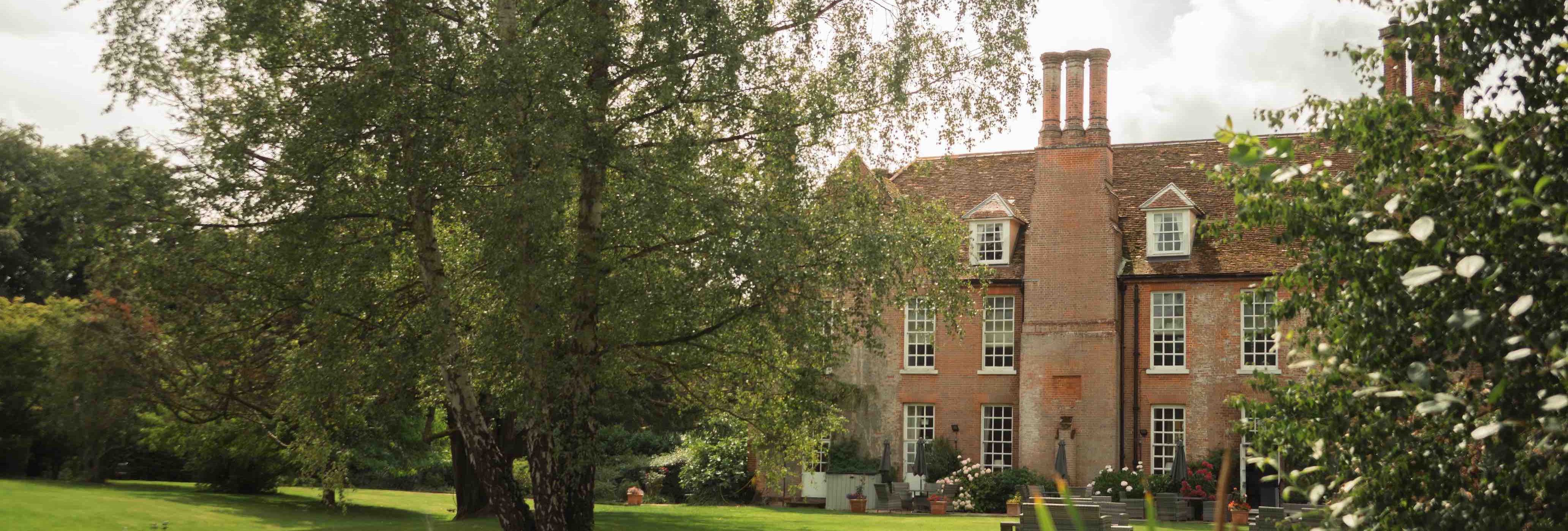 Large brick house with multiple chimneys, surrounded by a lush garden and pond