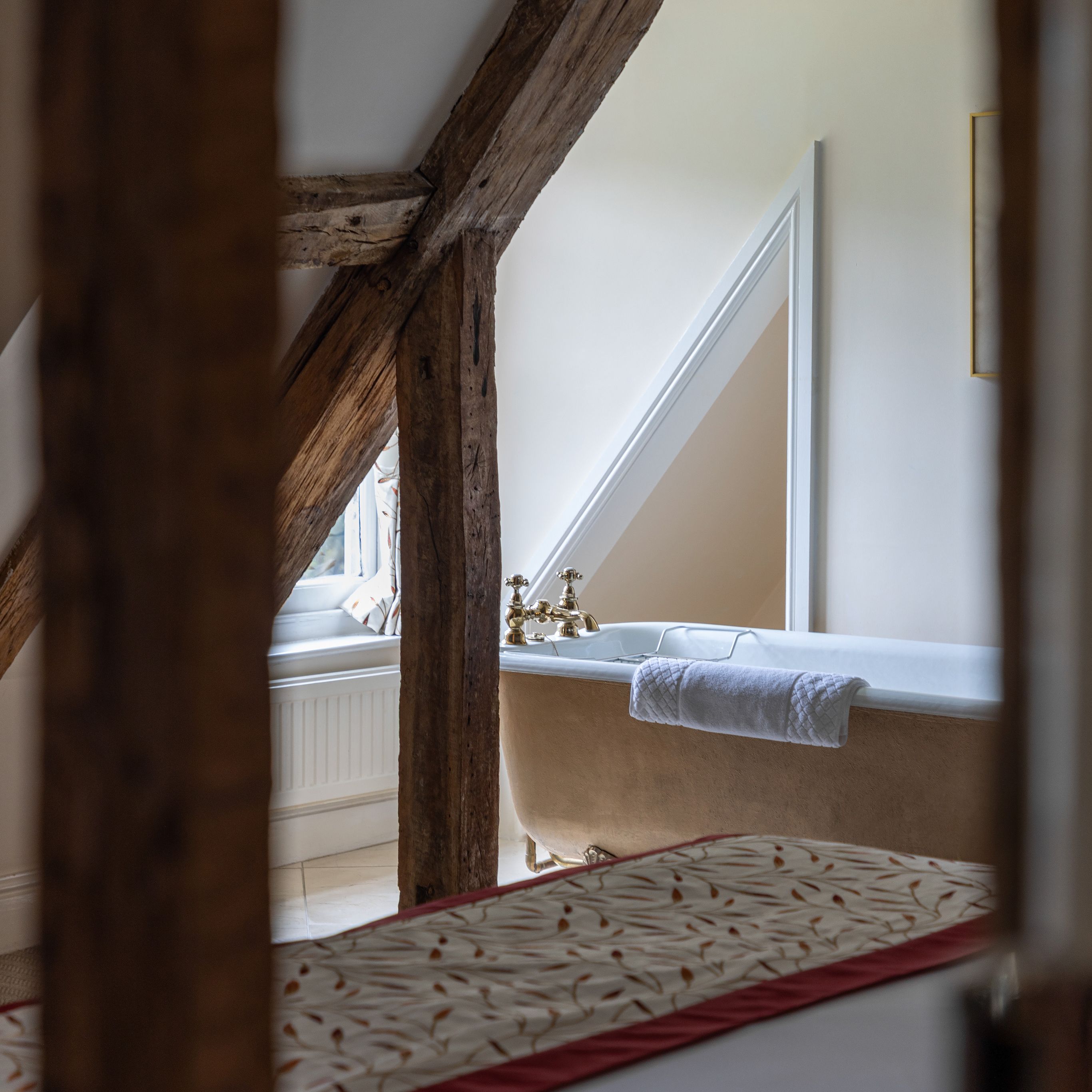 Rustic bathroom with exposed wooden beams and a freestanding bathtub under a slanted ceiling.