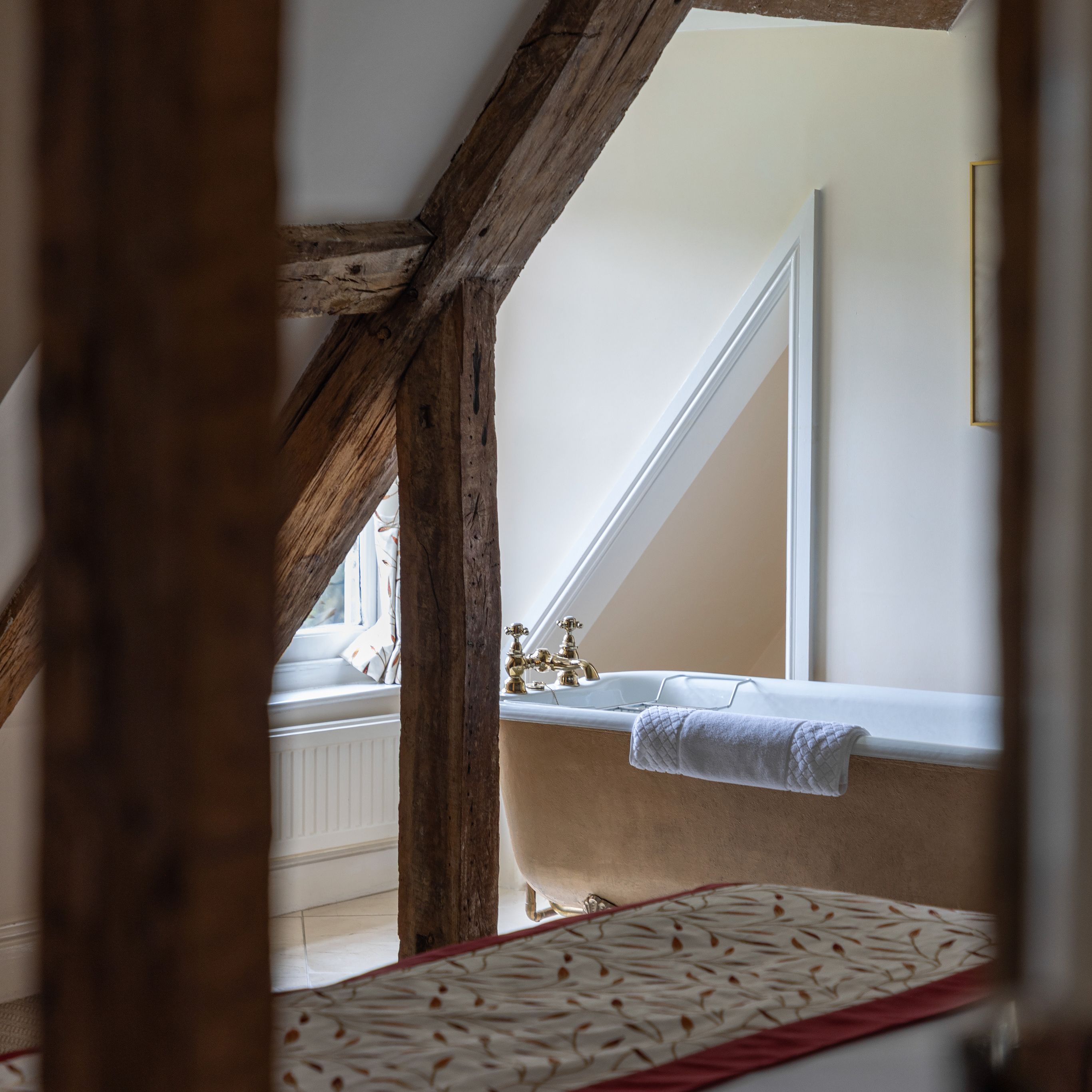 Rustic bathroom with exposed wooden beams and a freestanding bathtub under a slanted ceiling.