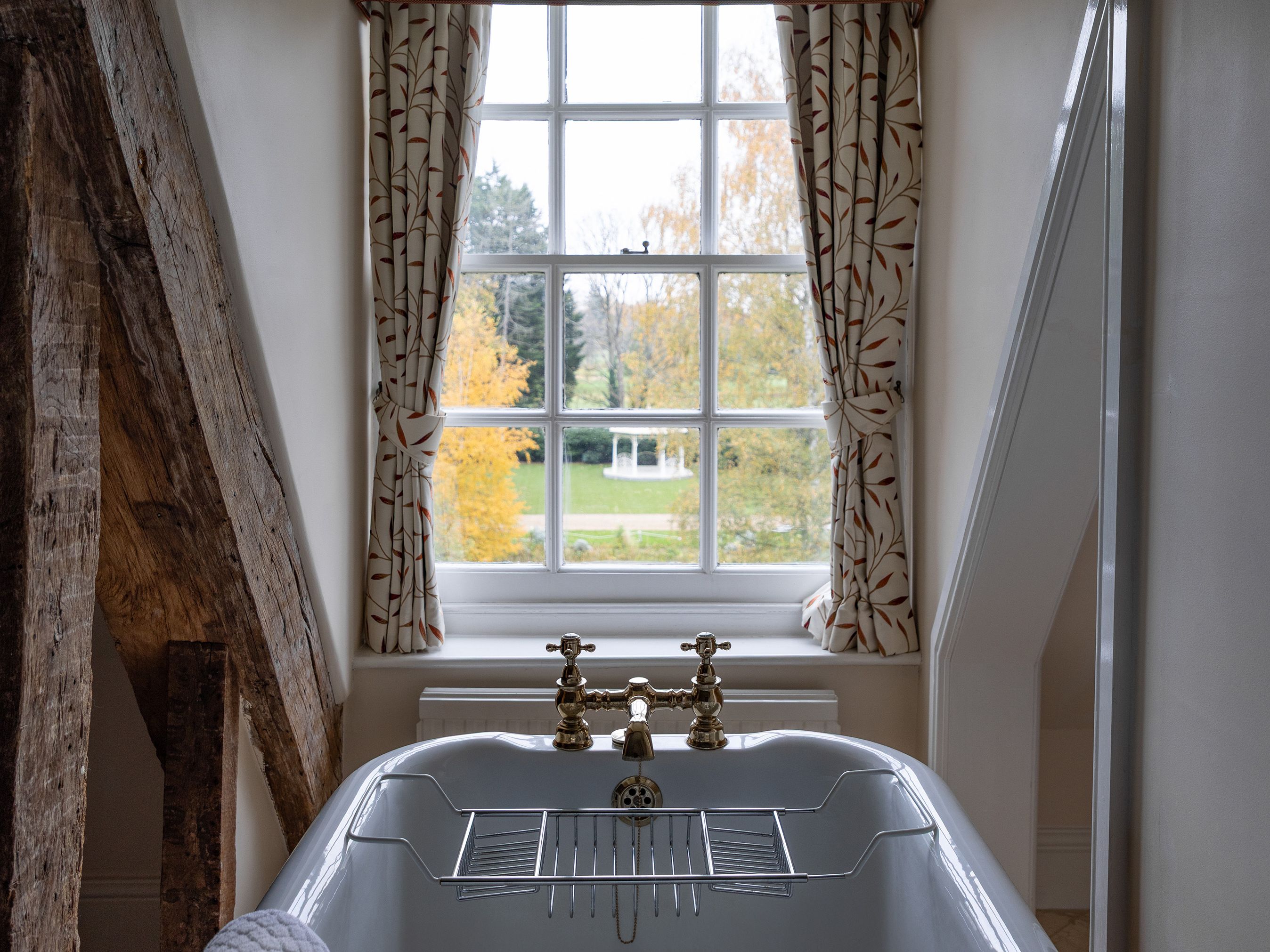 Freestanding bathtub in front of a window with patterned curtains in a cozy bathroom