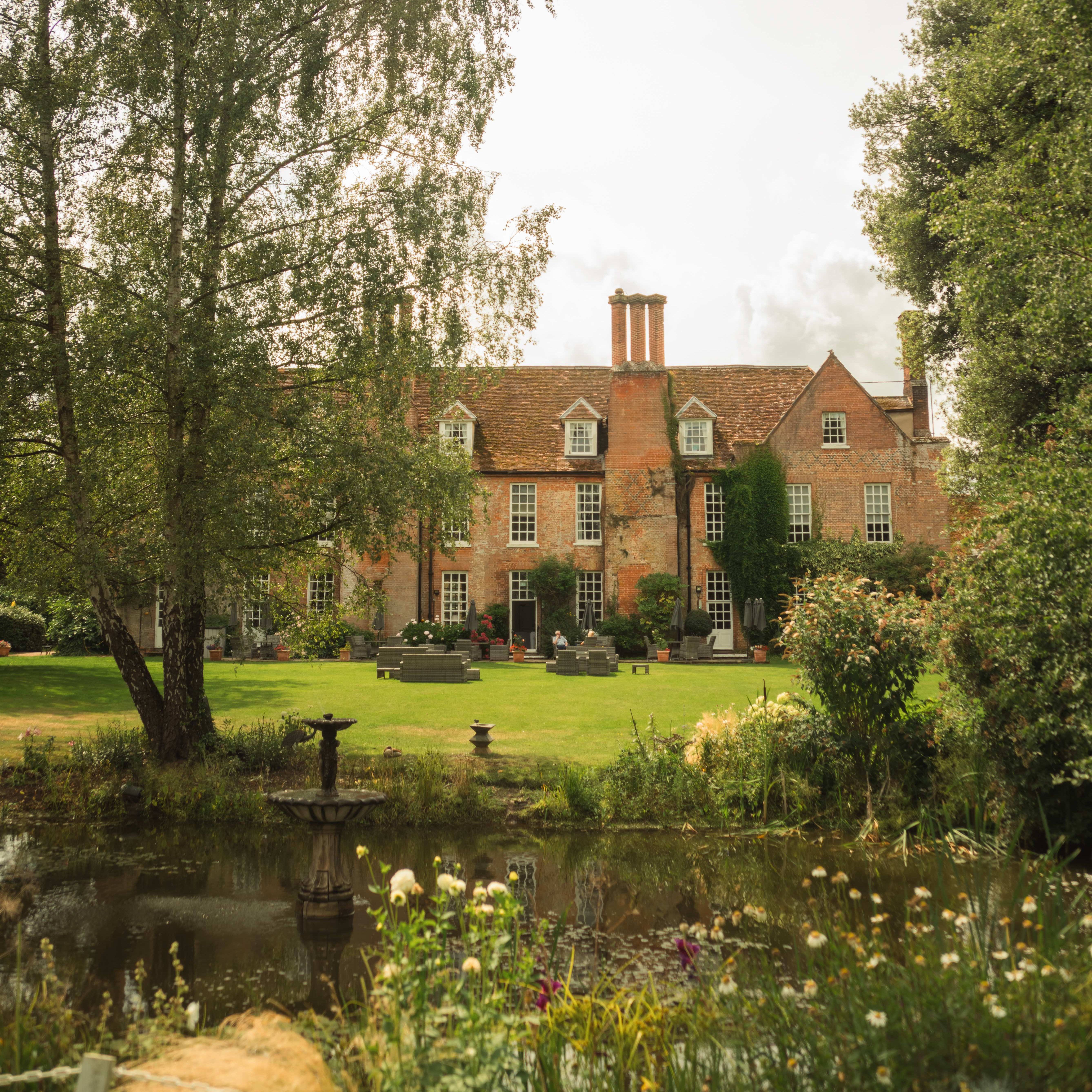 Historic brick manor house with large garden and pond in the foreground.