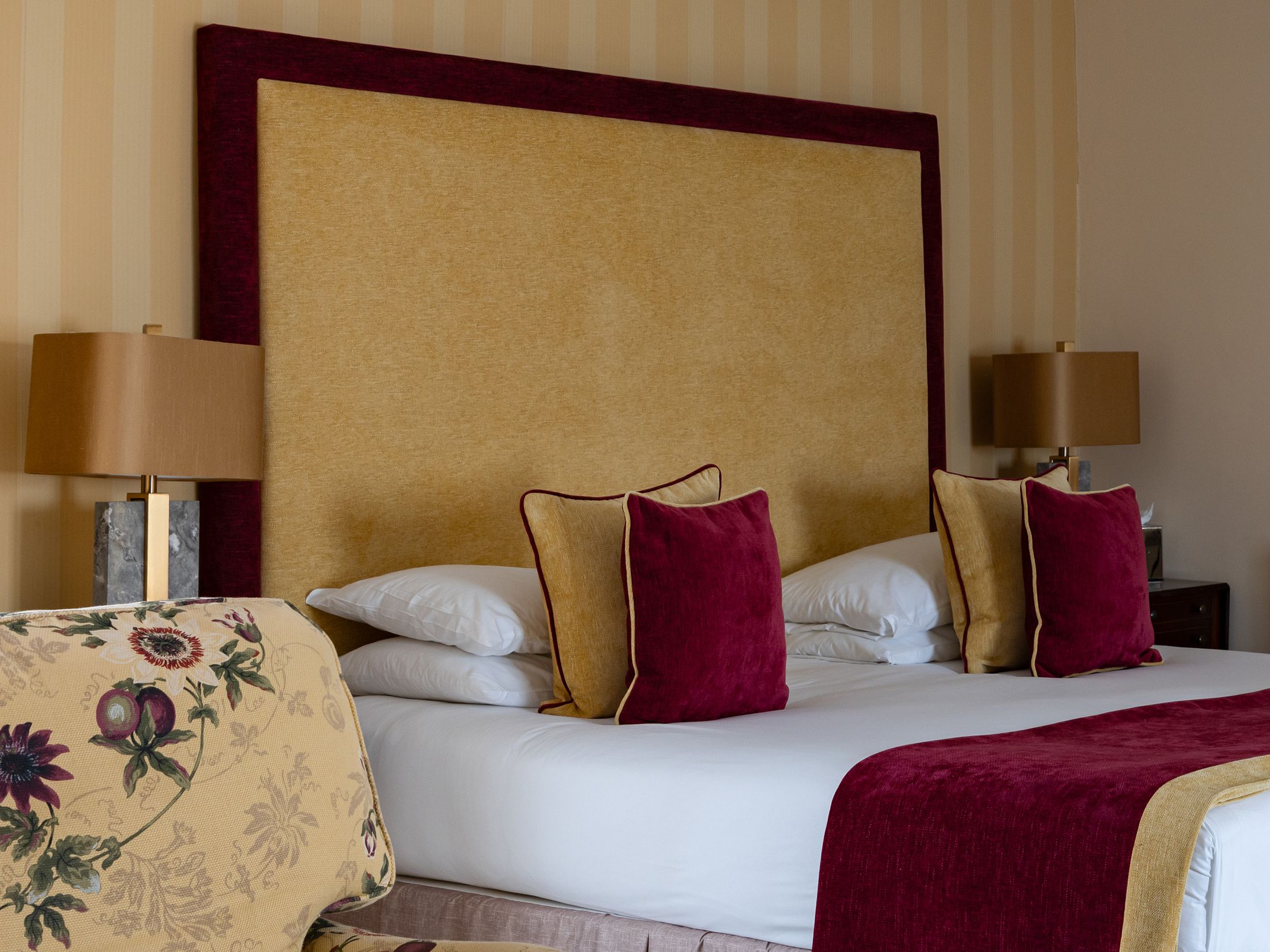 Elegant hotel room with a large bed, floral armchair, and striped wallpaper