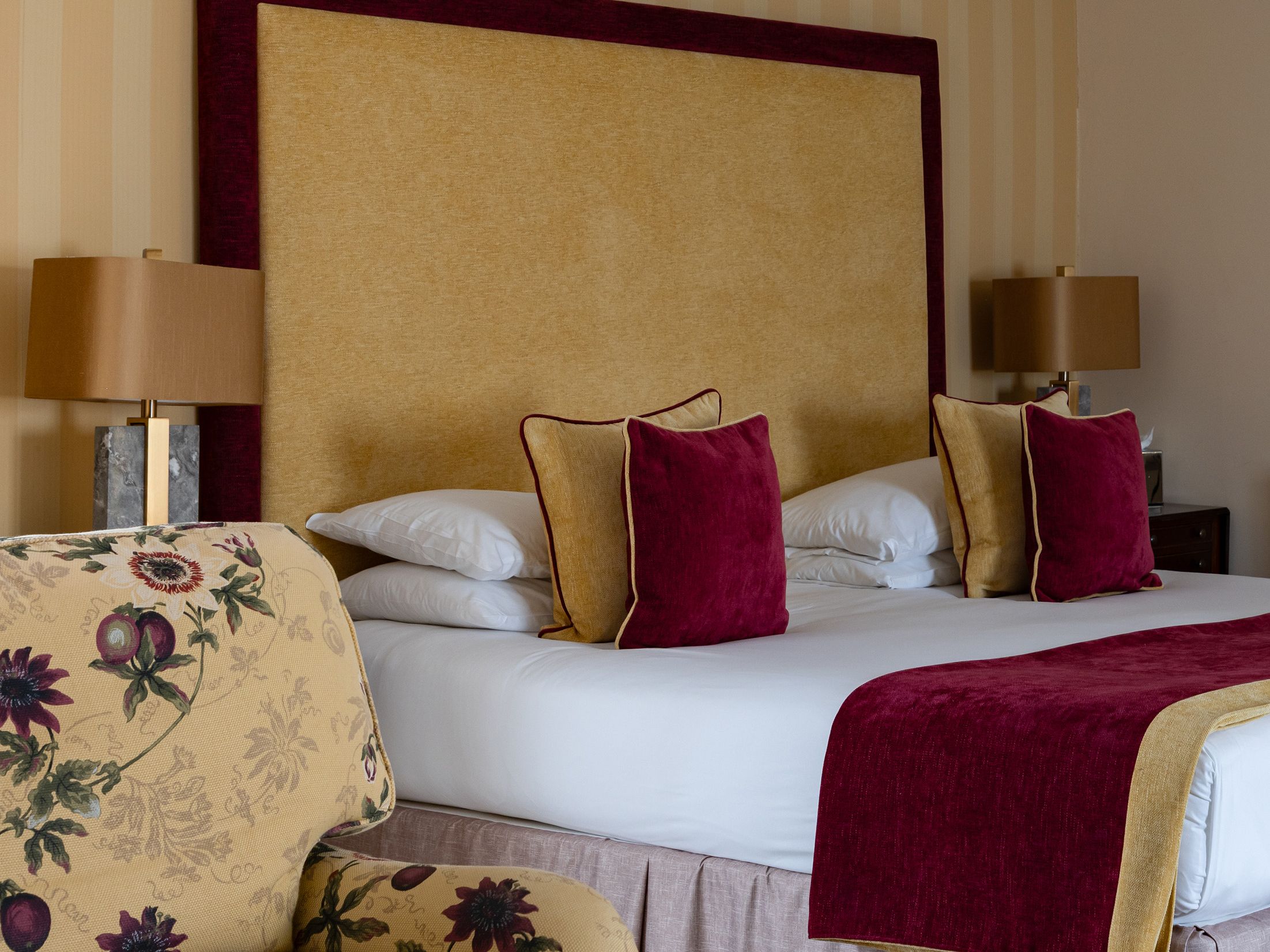 Elegant hotel room with a large bed, floral armchair, and striped wallpaper