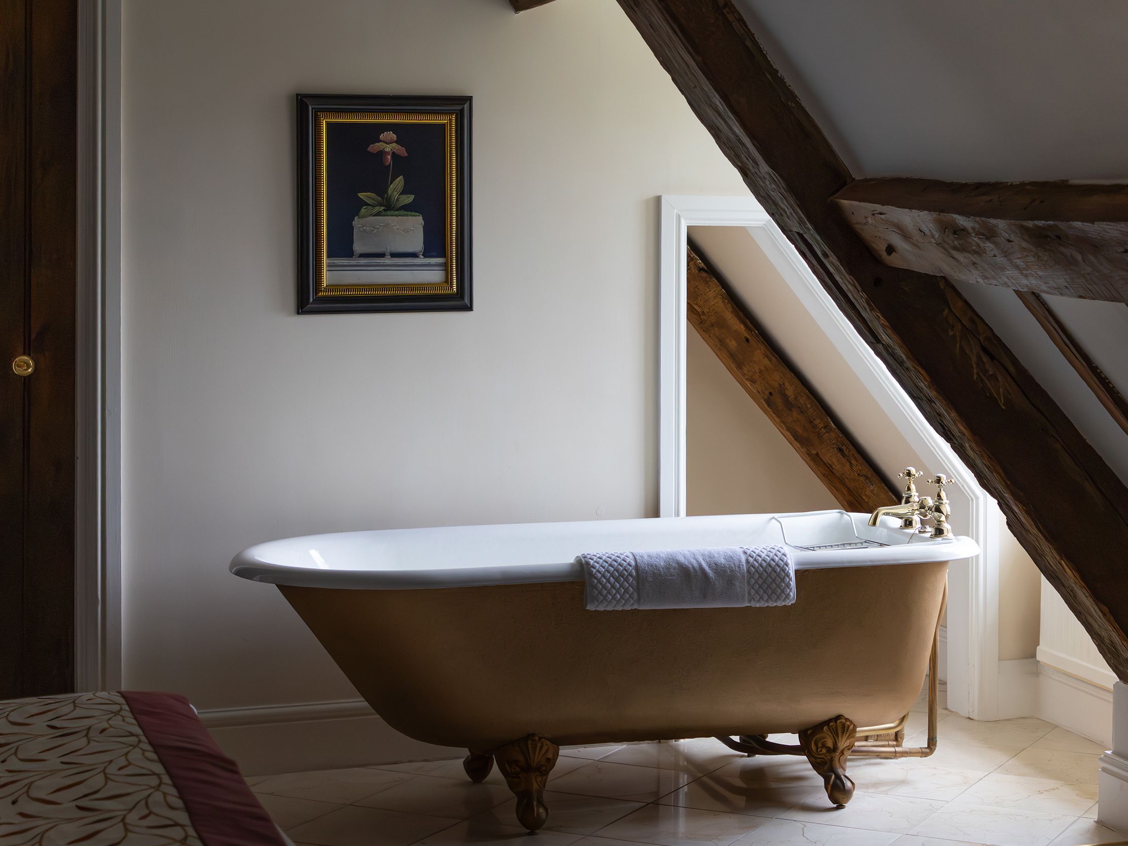 Vintage clawfoot bathtub beneath sloped ceiling and wooden beams in a cozy bathroom.