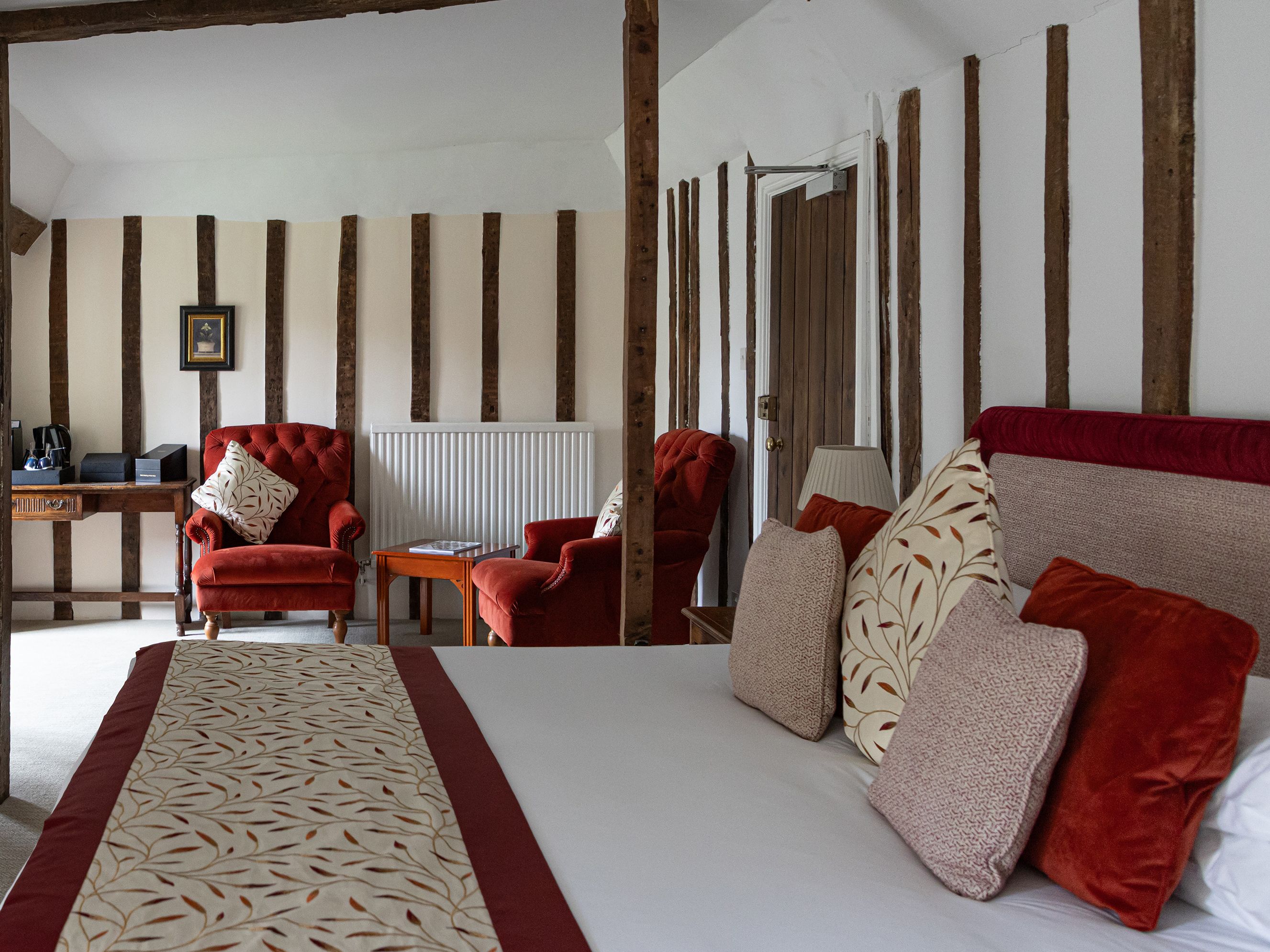 Cozy bedroom with red armchairs, decorative cushions, and exposed wooden beams