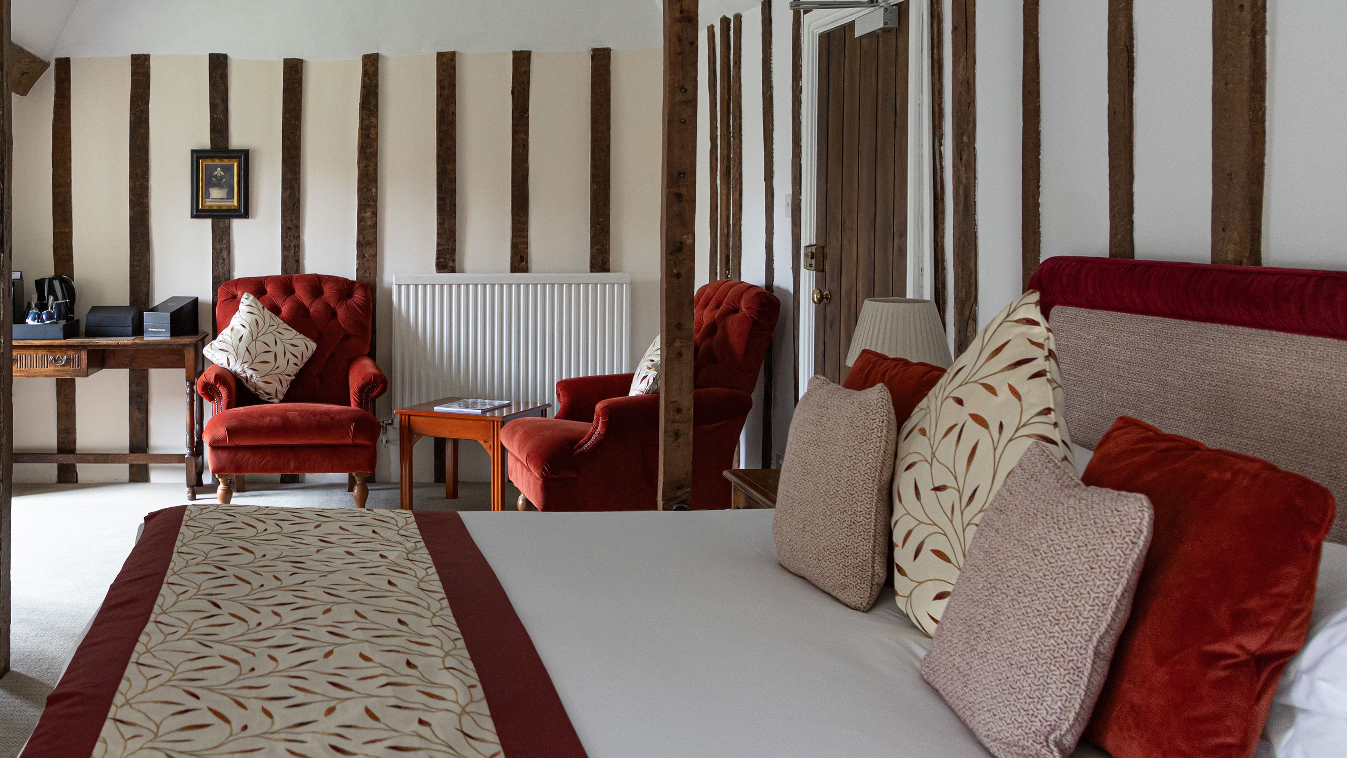 Cozy bedroom with red armchairs, decorative cushions, and exposed wooden beams
