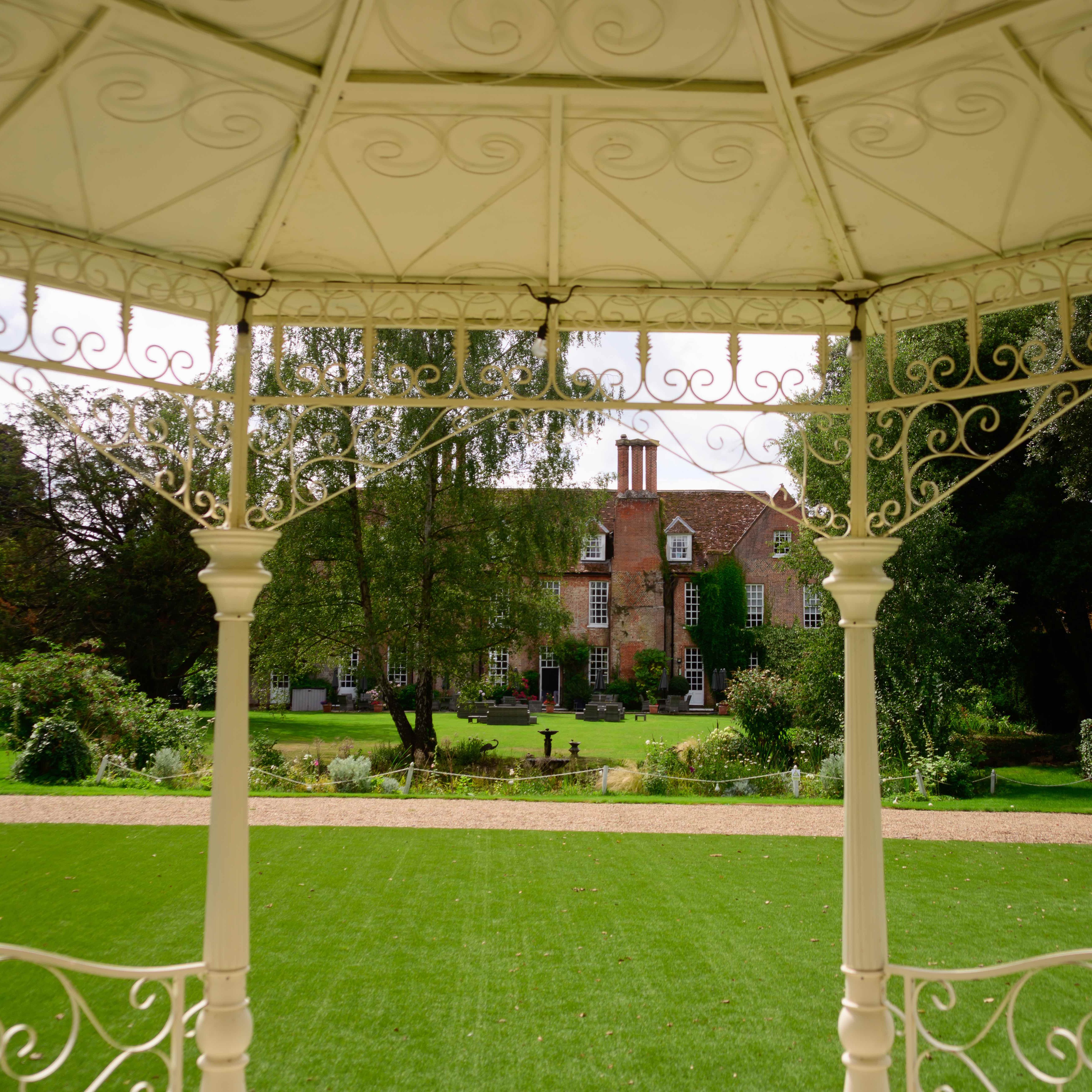 View from a gazebo looking onto a large garden with a historic brick mansion in the background.
