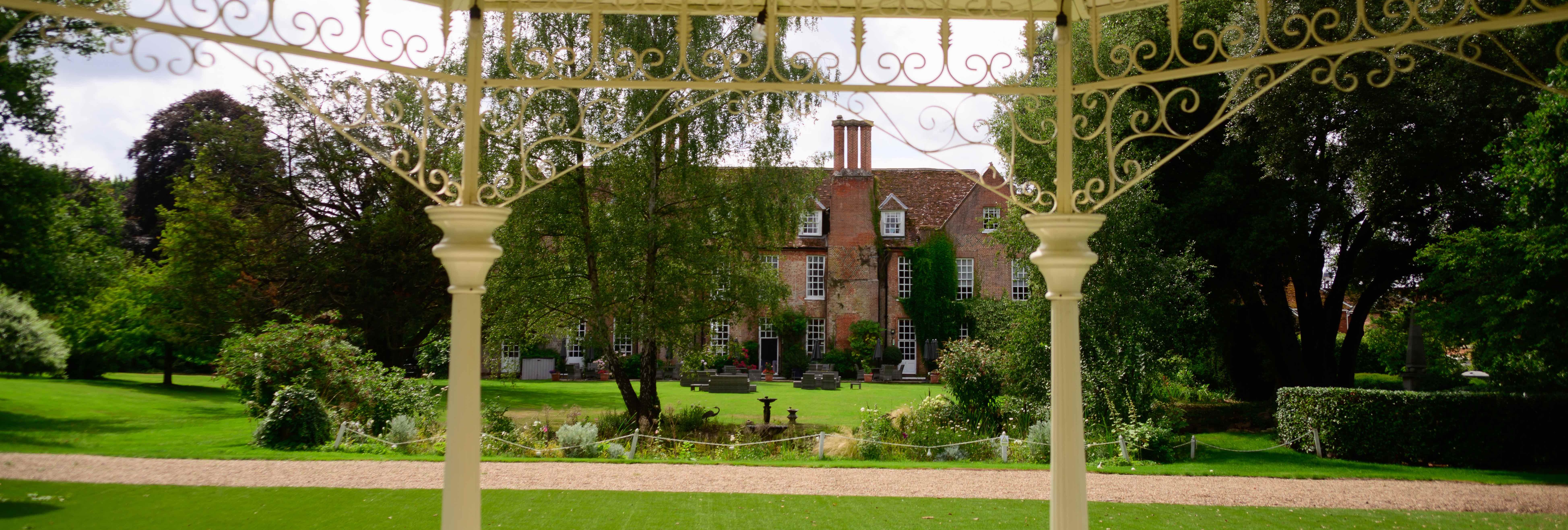 View from a gazebo looking onto a large garden with a historic brick mansion in the background.
